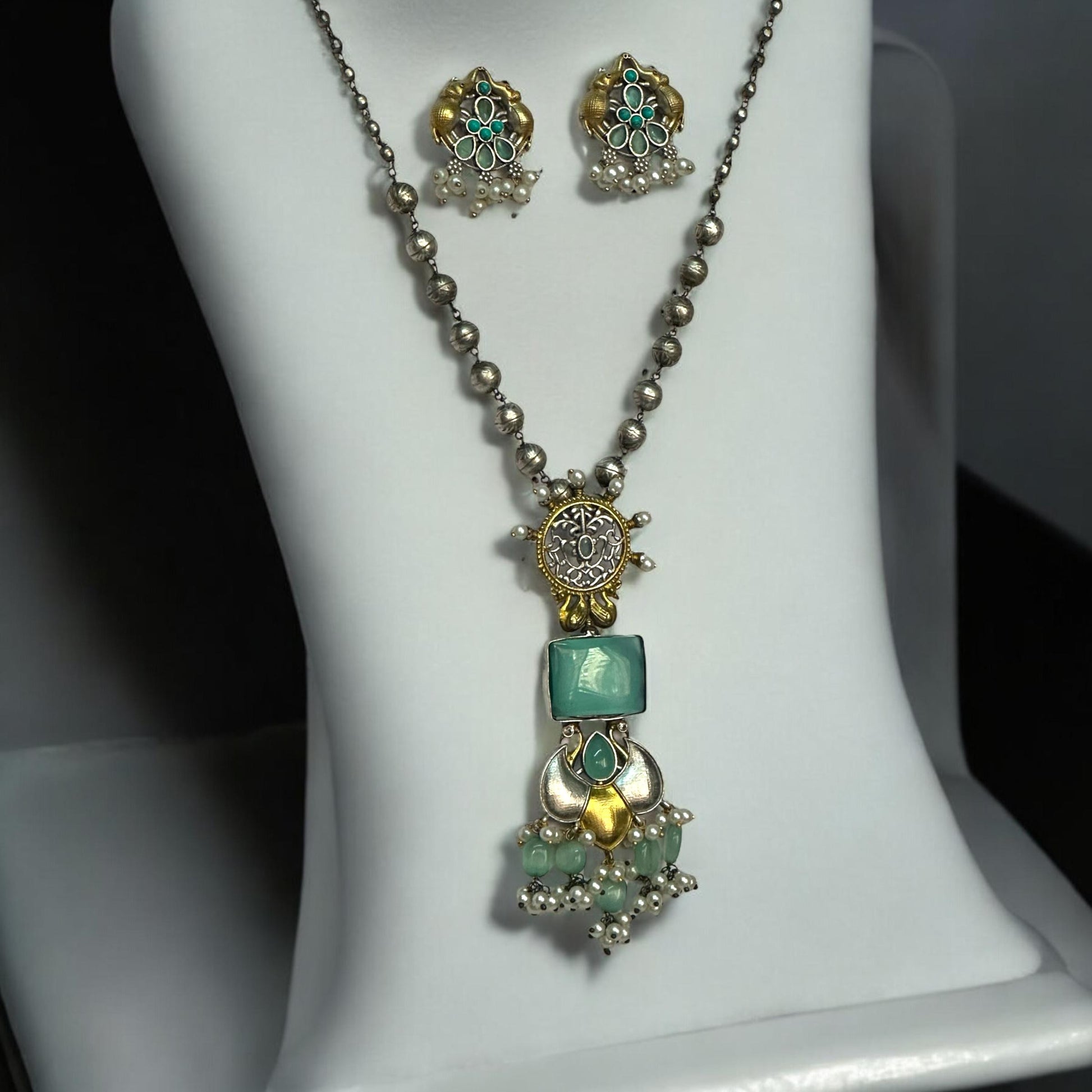 Dual Tone Silver Replica Long Matar Mala Design Necklace Set featuring sky-colored stones and intricate dual-tone silver-gold craftsmanship, displayed on a white jewellery display stand against a soft black and white gradient background.