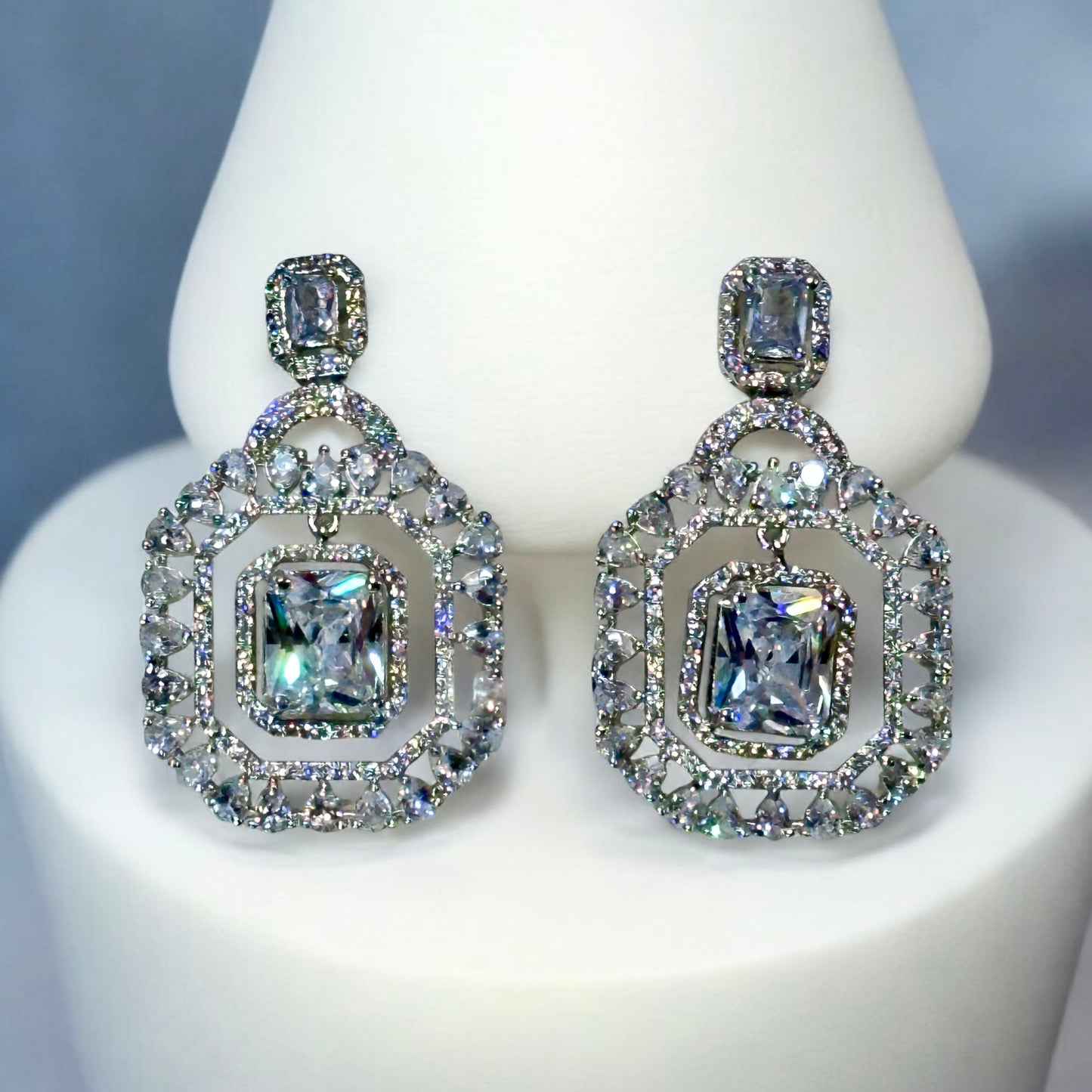A pair of an American Diamonds Statement Earring on a white coloured jewellery display stand.