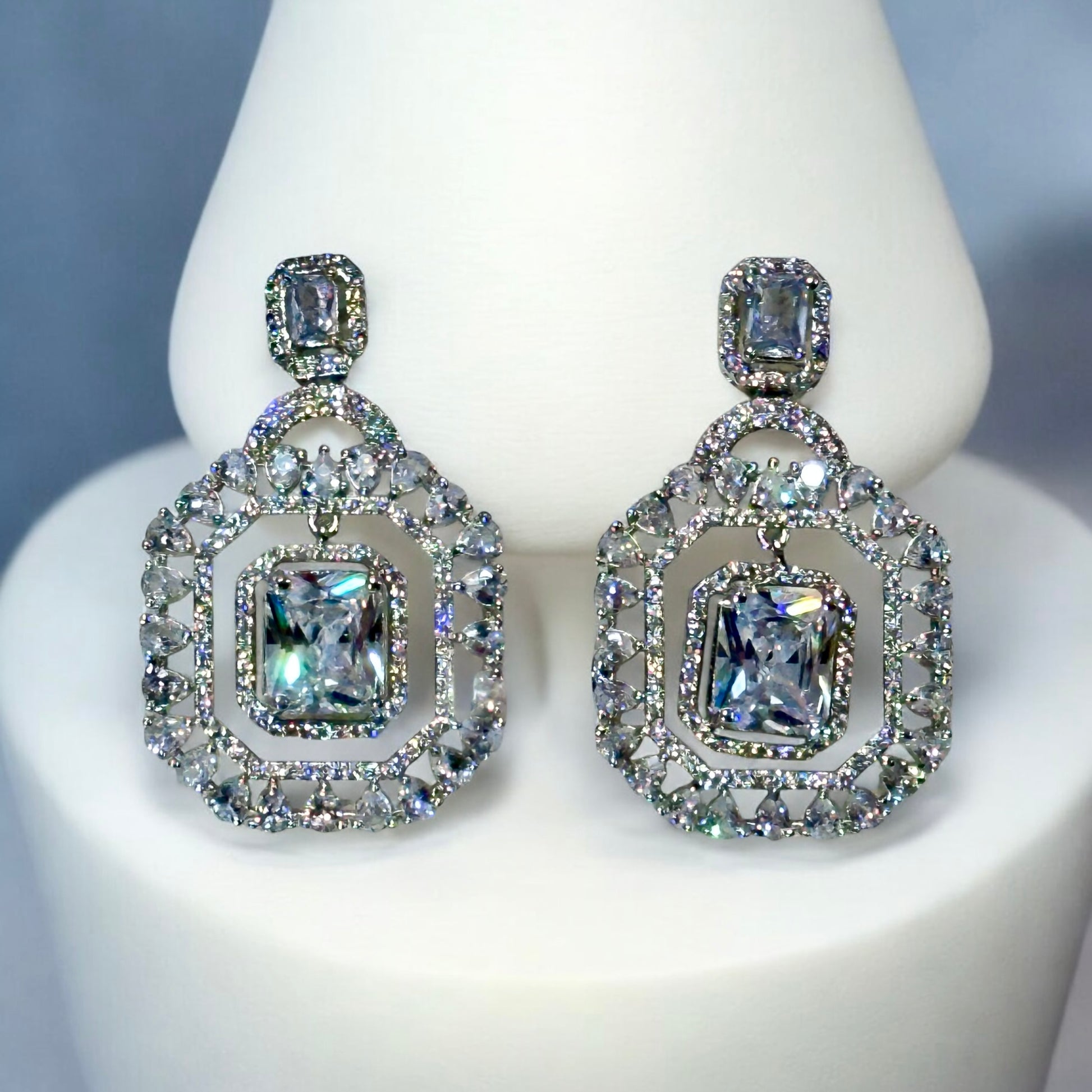 A pair of an American Diamonds Statement Earring on a white coloured jewellery display stand.