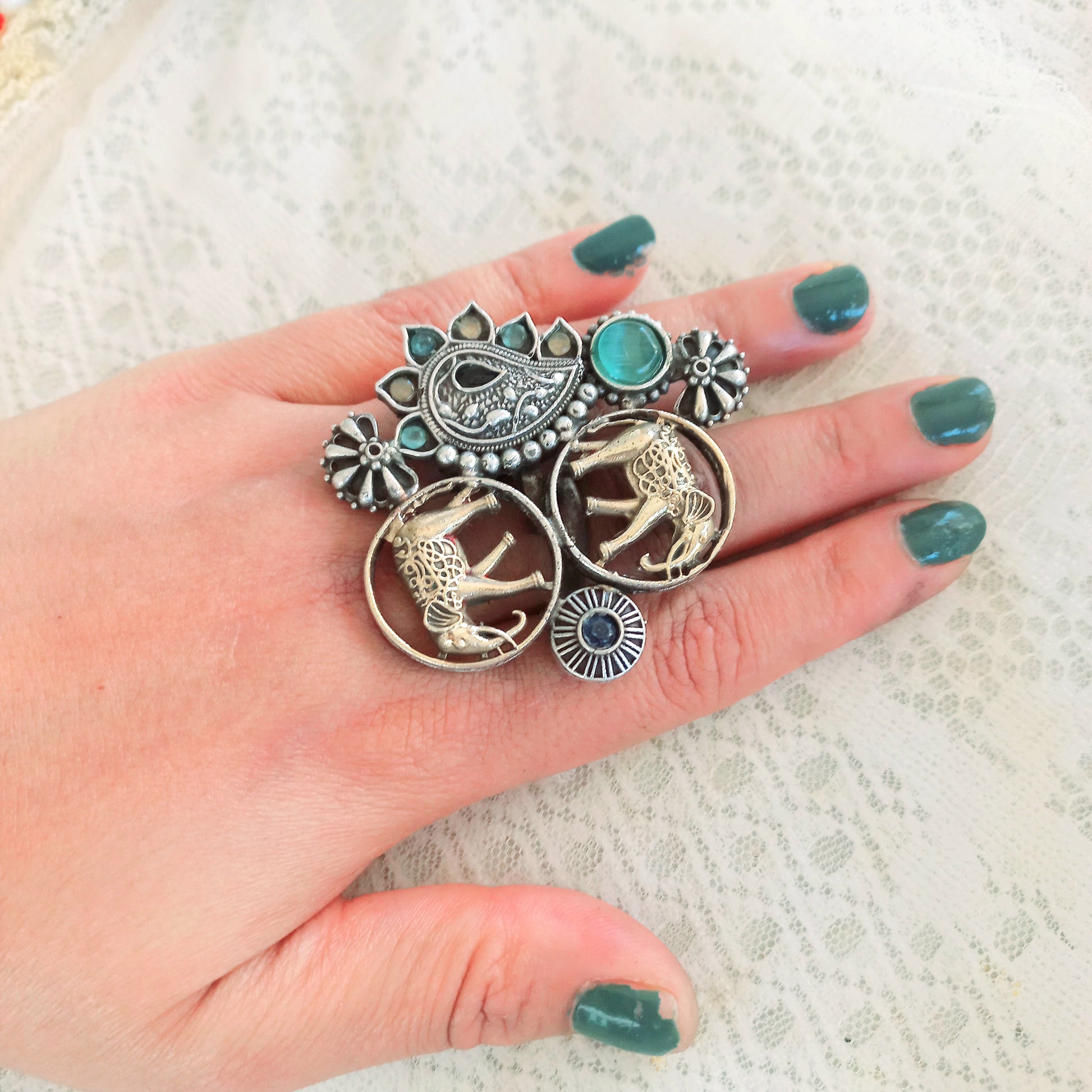 An Elephant Design Oxidised Fusion Finger Ring, featuring intricate oxidised silver detailing, a regal elephant motif, and gemstone embellishments, worn on a hand with green-painted nails over a lace fabric background.