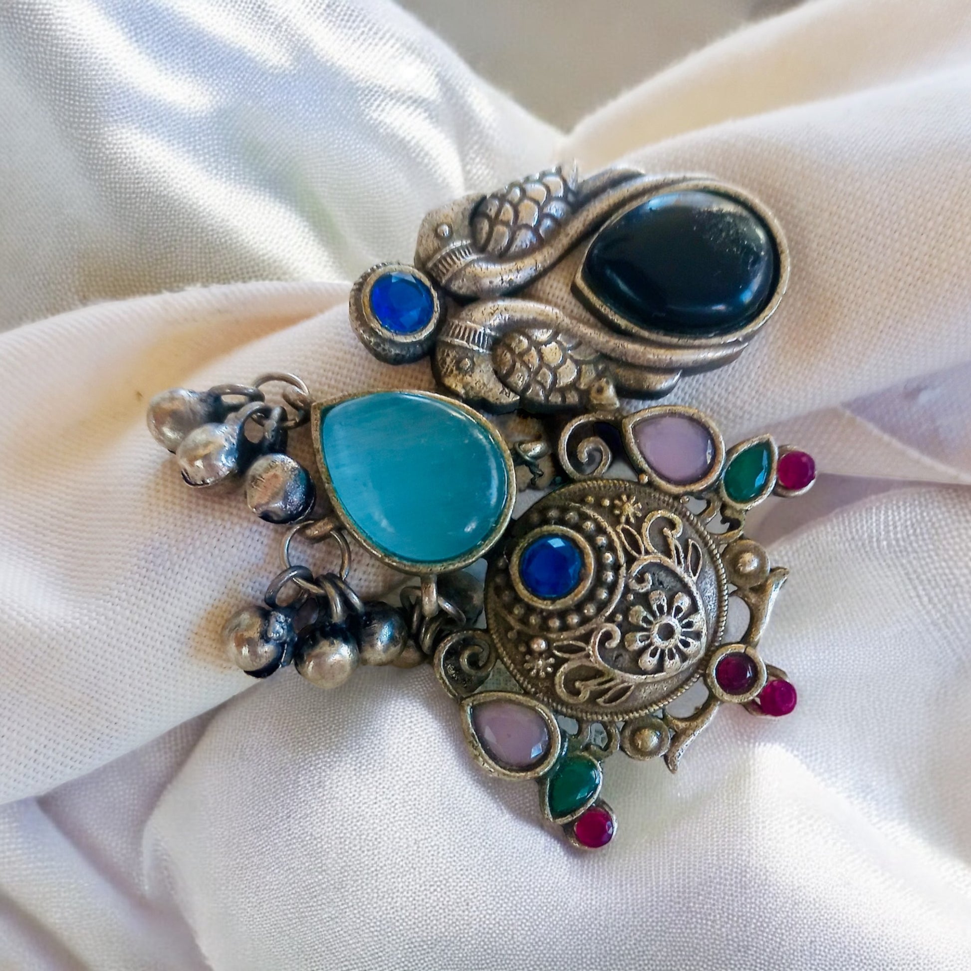 A handcrafted Fusion Finger Ring Designer Adjustable, featuring intricate silver detailing, vibrant gemstones, and a unique artistic design, worn on a fabric over a lace fabric background.