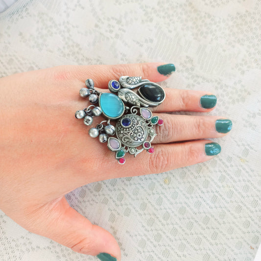 A handcrafted Fusion Finger Ring Designer Adjustable, featuring intricate silver detailing, vibrant gemstones, and a unique artistic design, worn on a hand with green-painted nails over a lace fabric background.