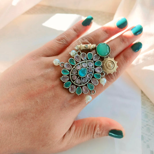 Fusion ring with multicolor gemstones on a hand model with green nail polish.
