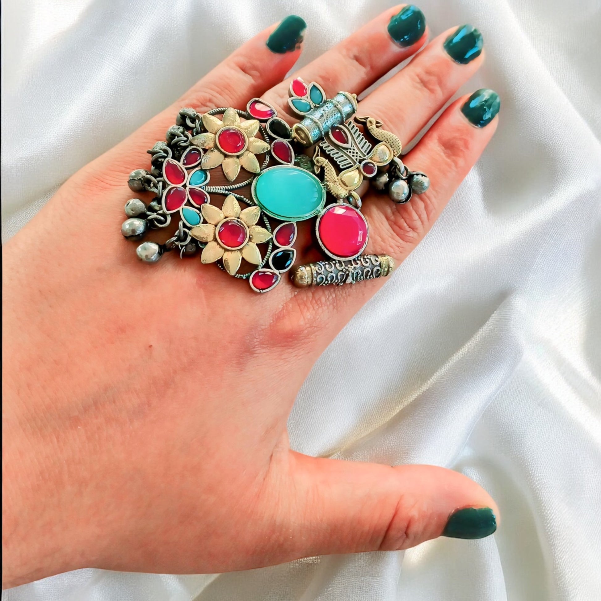 A woman's hand wearing a vibrant Fusion Silver Multi Color Adjustable Ring with antique silver finish and colourful stones, styled on a satin fabric background.