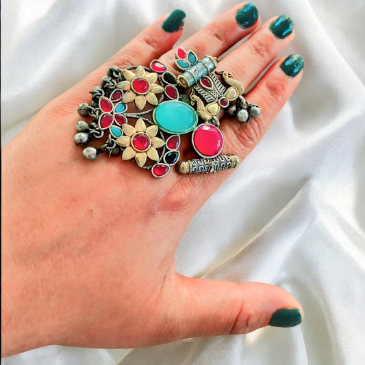 A woman's hand wearing a vibrant Fusion Silver Multi Color Adjustable Ring with antique silver finish and colourful stones, styled on a satin fabric background.
