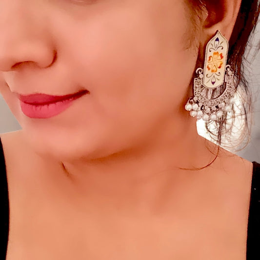 A model displaying Fusion Hand Painted Statement Earrings with intricate floral motifs, vintage silver detailing, and pearl embellishments, displayed on a white stand.