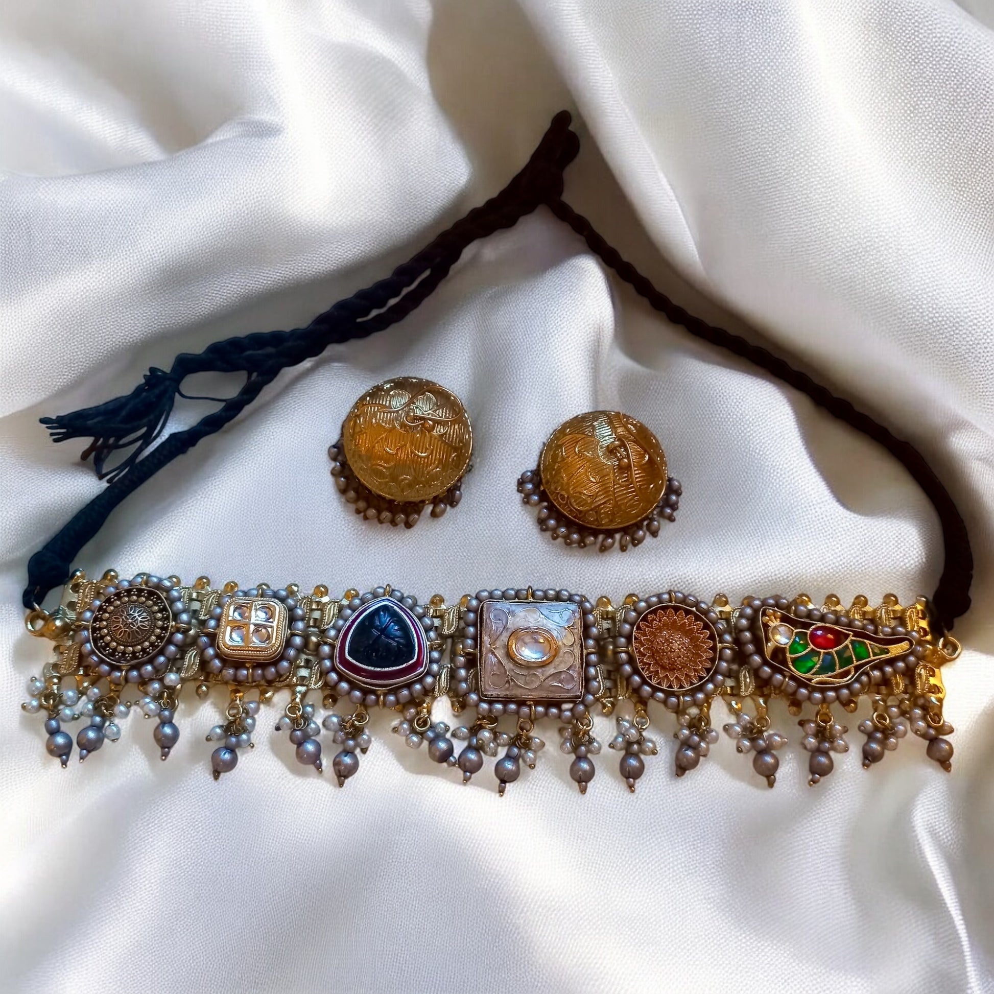 Fusion Pachi Kundan choker with pearls and colourful motifs paired with antique gold dome jhumkas on a white fabric background