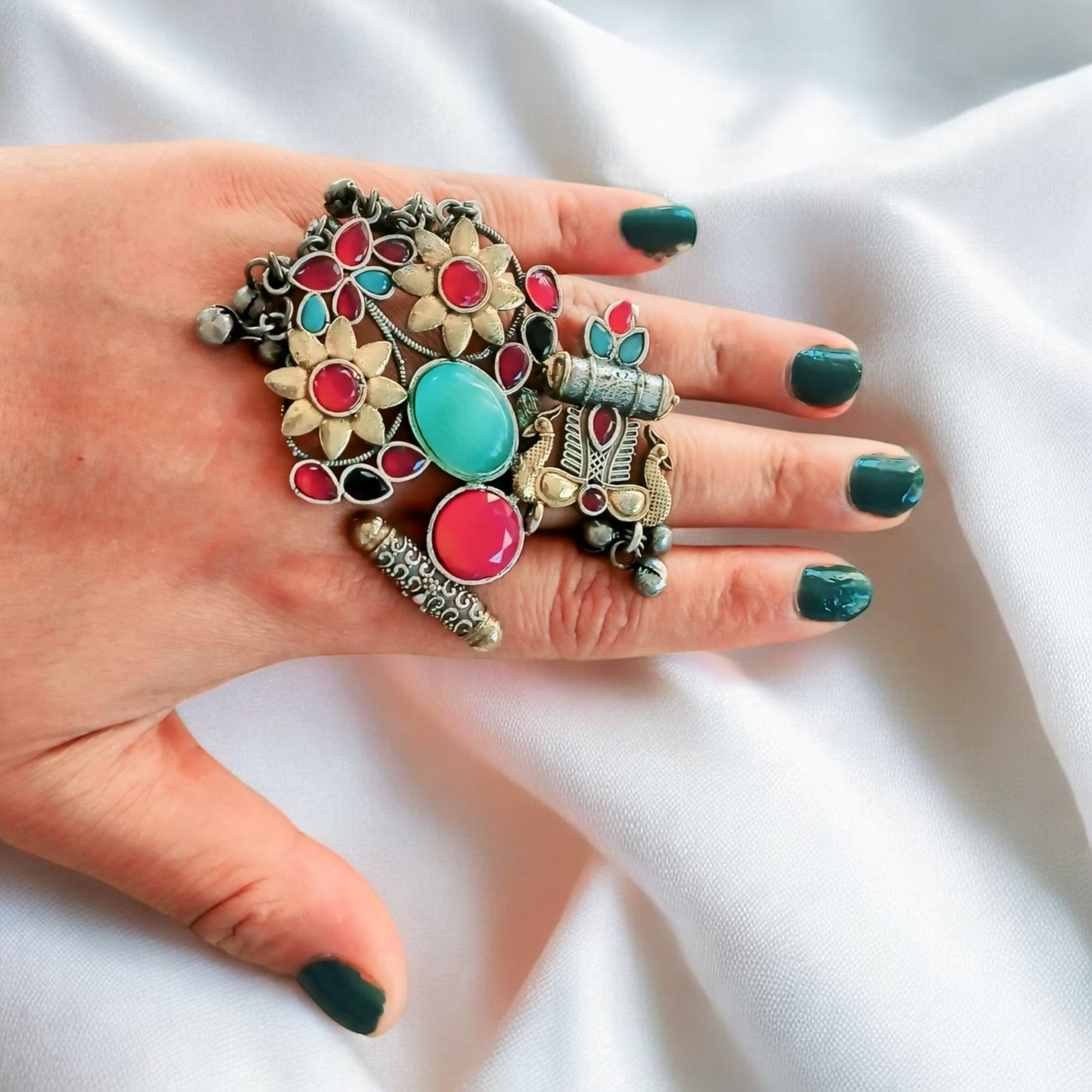 A woman's hand wearing a vibrant Fusion Silver Multi Color Adjustable Ring with antique silver finish and colourful stones, styled on a satin fabric background.