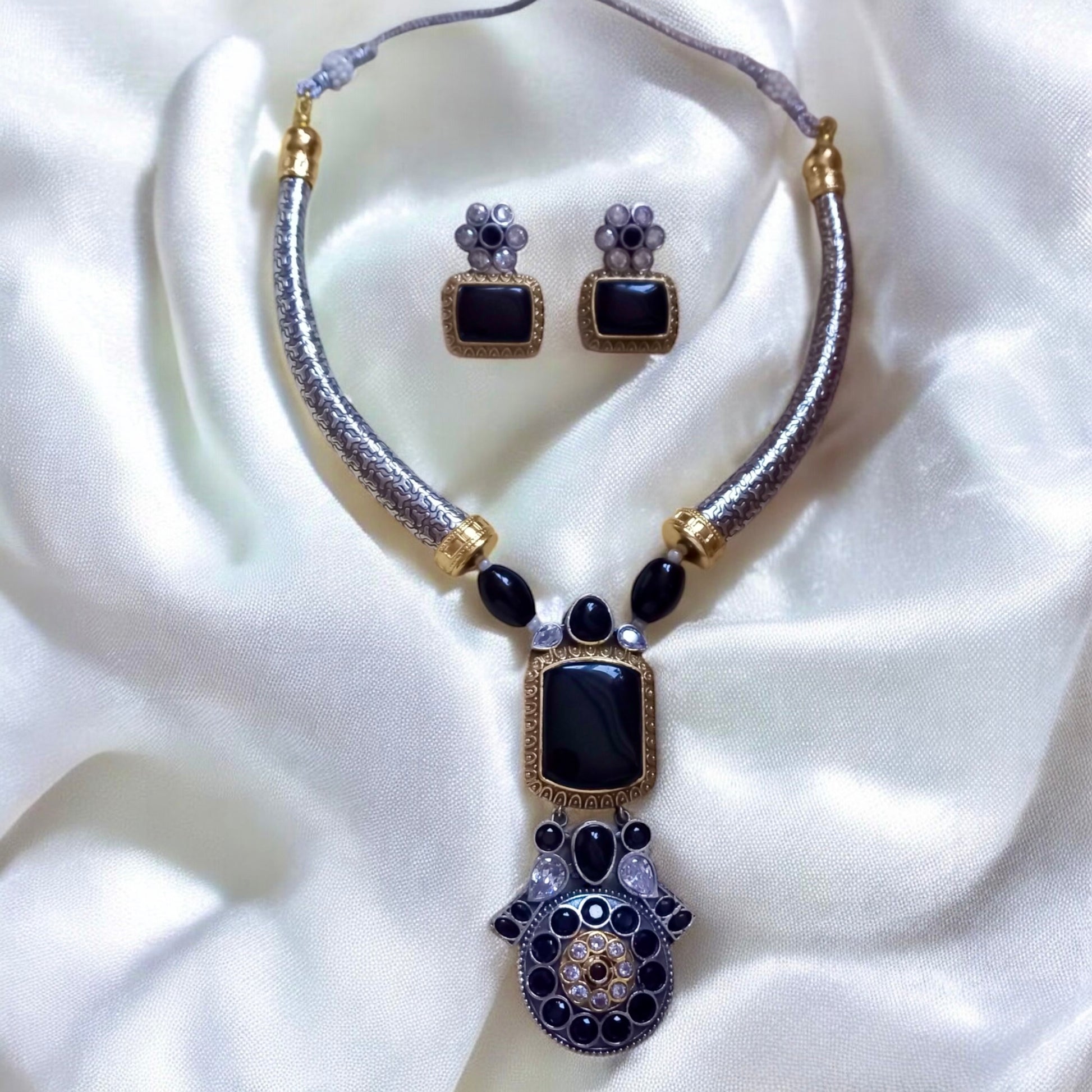 German silver hasli necklace with black Monalisa stones and antique oxidised pendant, paired with matching square black earrings on cream satin background
