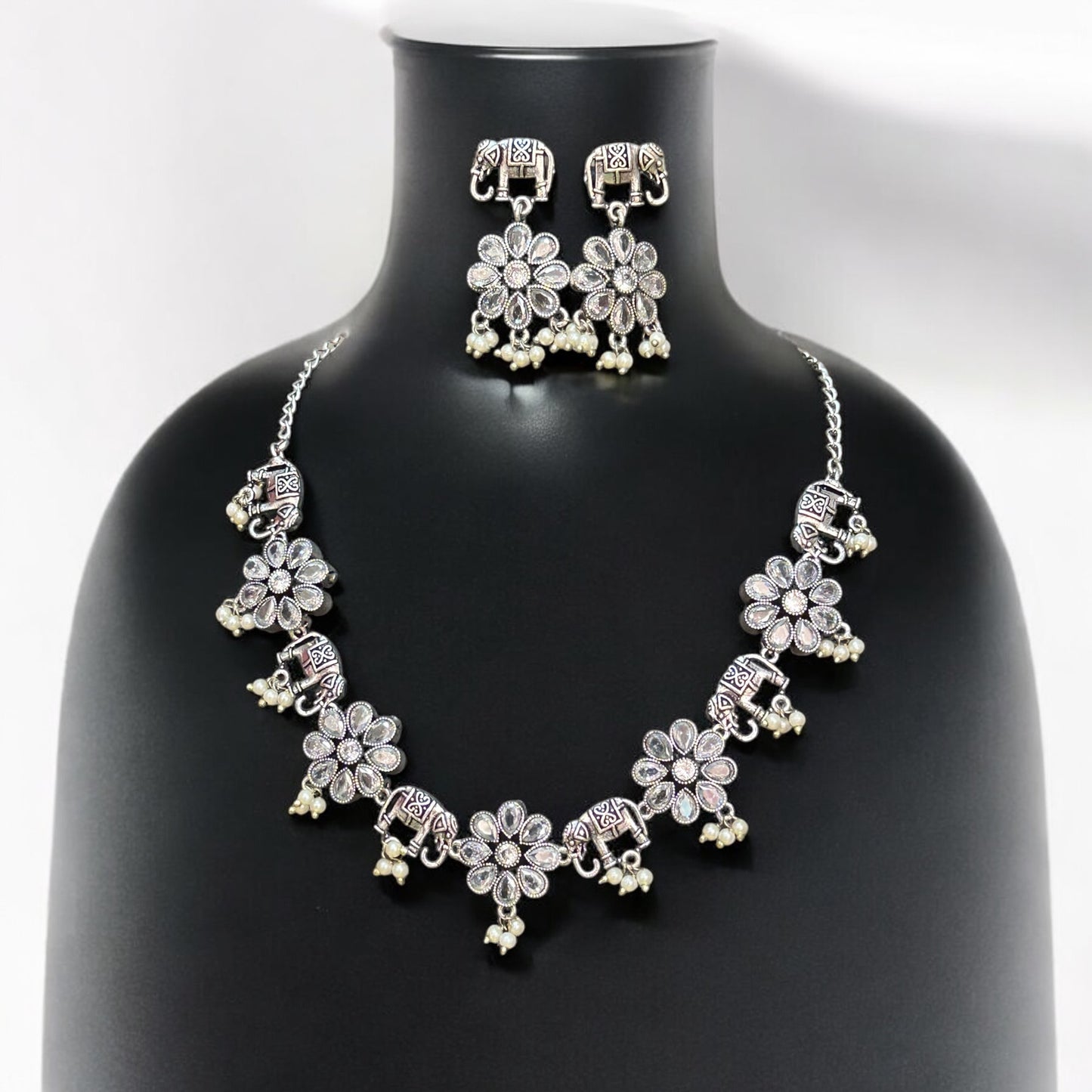 German silver necklace set in elephant and floral design with white bead drops and matching oxidised earrings displayed on black mannequin