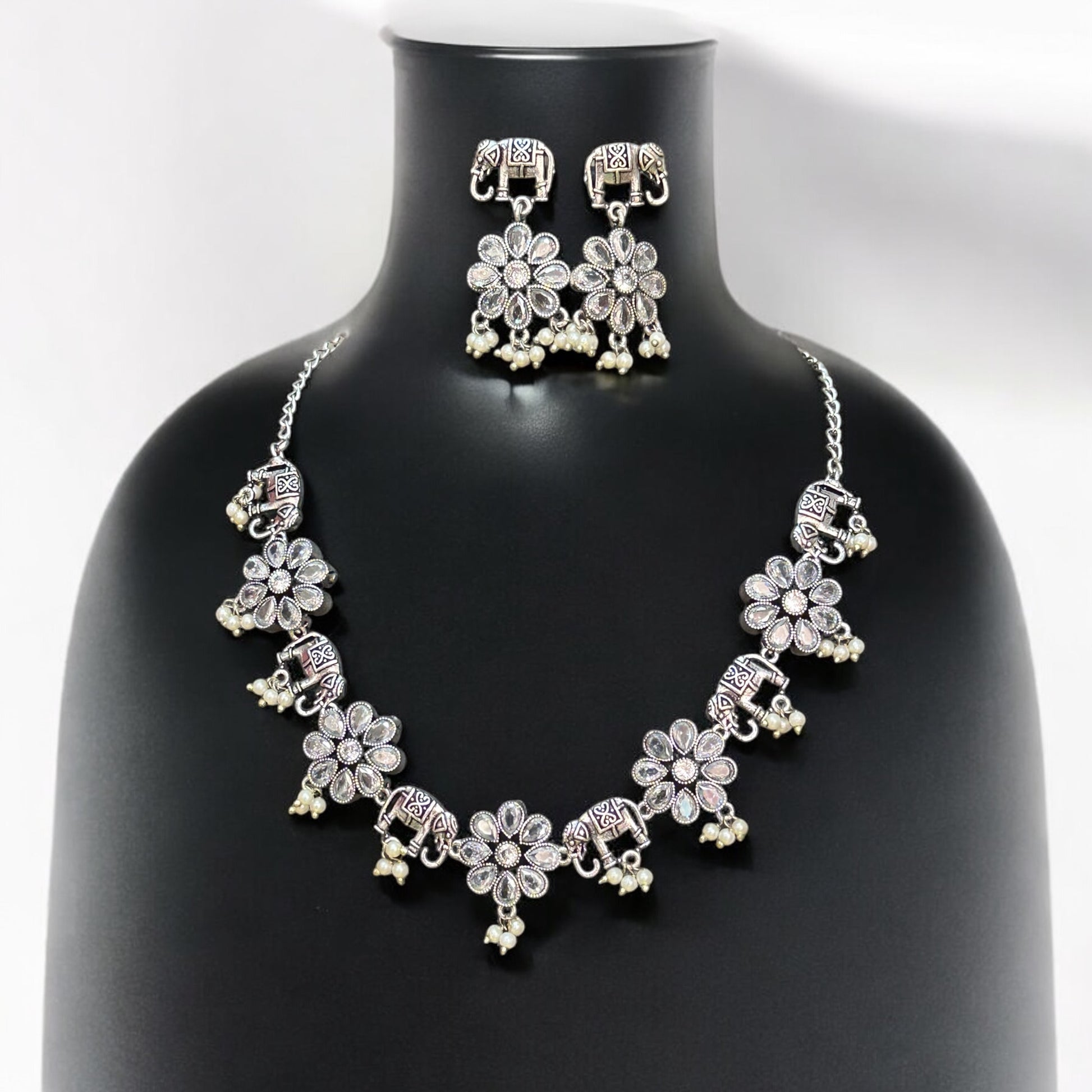 German silver necklace set in elephant and floral design with white bead drops and matching oxidised earrings displayed on black mannequin