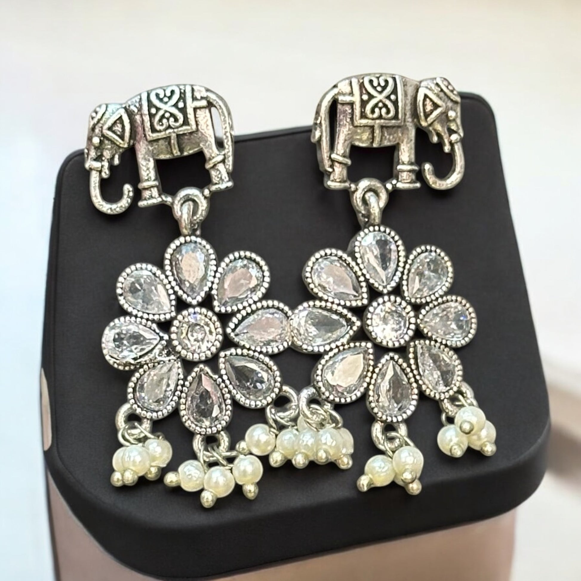 German silver earrings featuring intricate elephant motifs and floral design adorned with dangling pearls. Displayed on a black mannequin bust against a plain background.