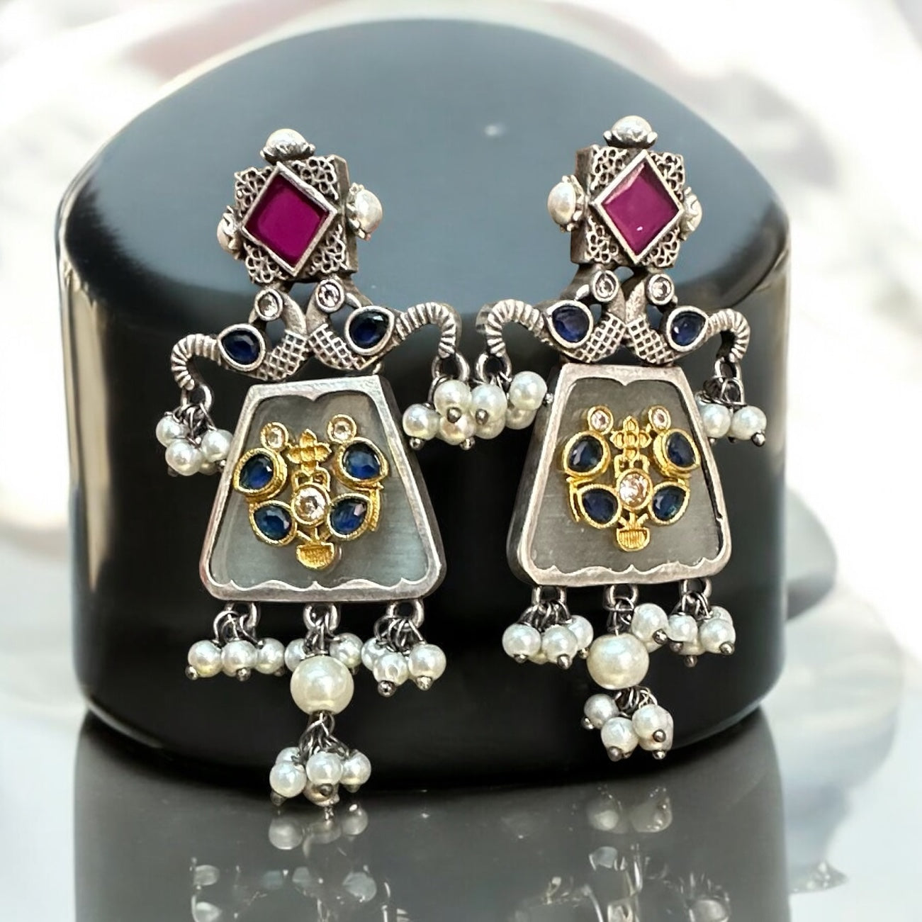 German silver replica statement Earrings featuring floral motifs in gold and pink highlights, displayed on a black jewellery display stand, elegant background.