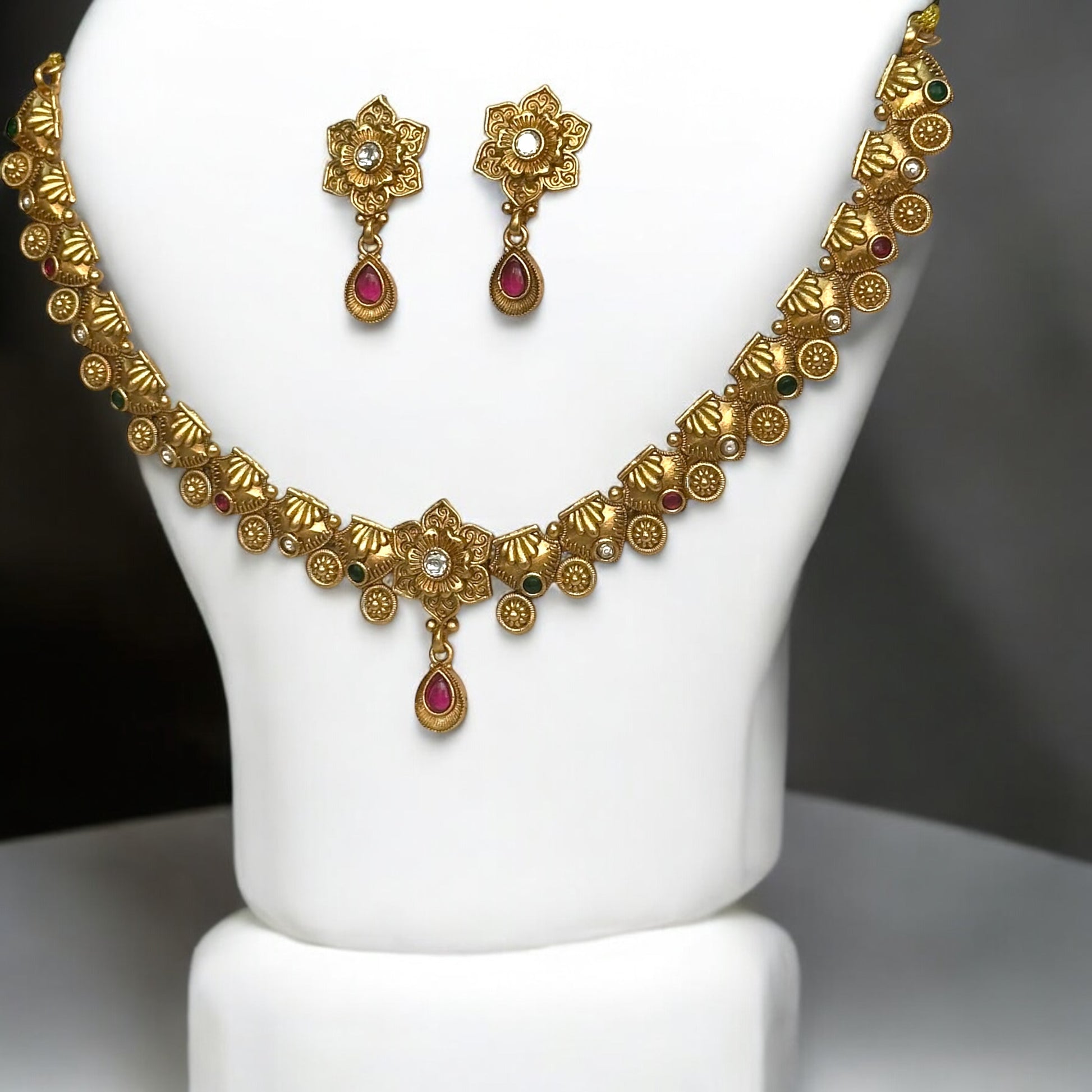 Golden Rajwadi Minimal Necklace Set featuring an intricately detailed necklace adorned with tiny floral and gemstone accents, paired with matching earrings. Displayed on a white bust stand against a soft background.