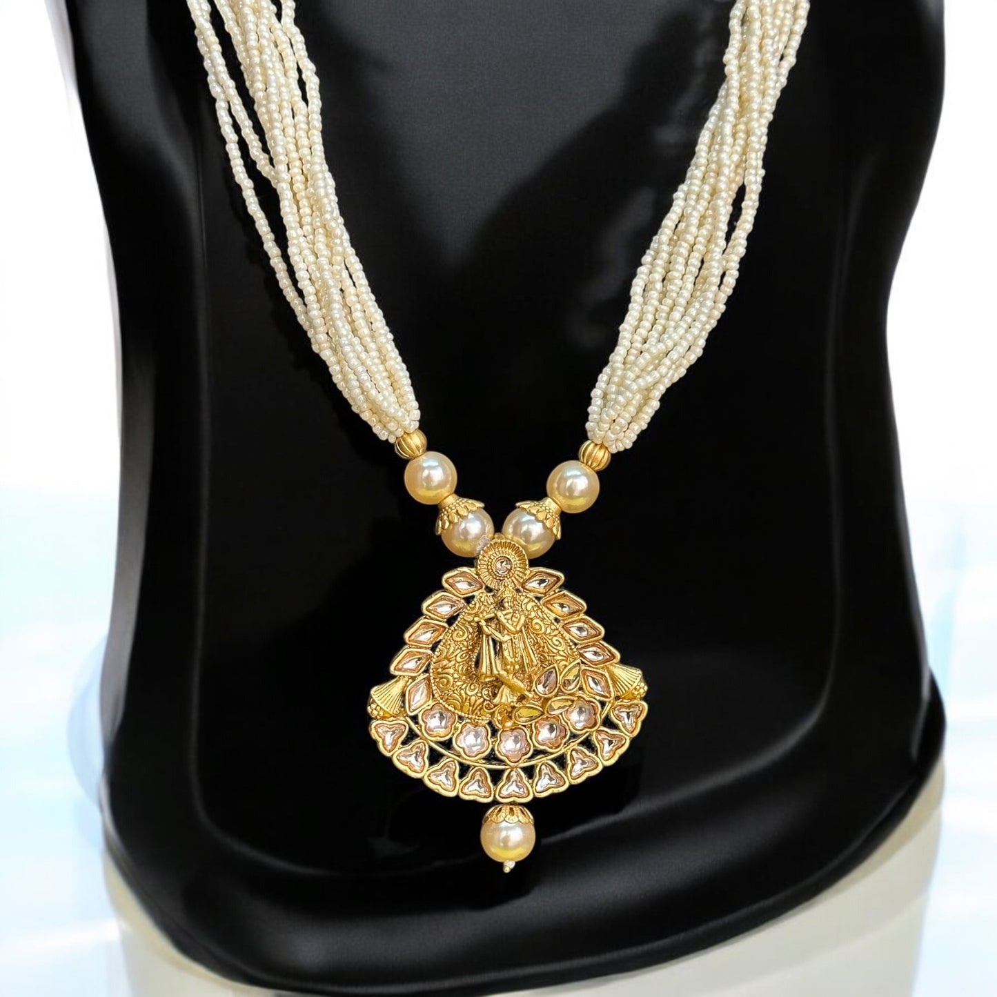 Pearl Mala with Krishna Design featuring multi-layered pearl strands and a gold-toned pendant intricately depicting Lord Krishna. Displayed on a black stand, showcasing the elegant craftsmanship and divine design.