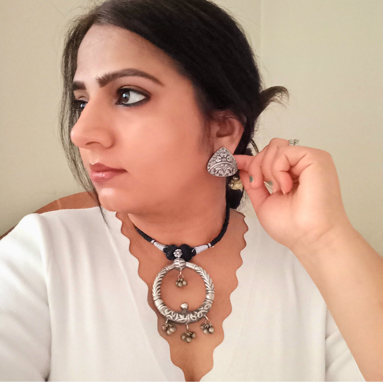 A model displaying Handmade silver replica necklace featuring a bold circular pendant with intricate engravings and ghungroo charms, paired with detailed triangular stud earrings. 