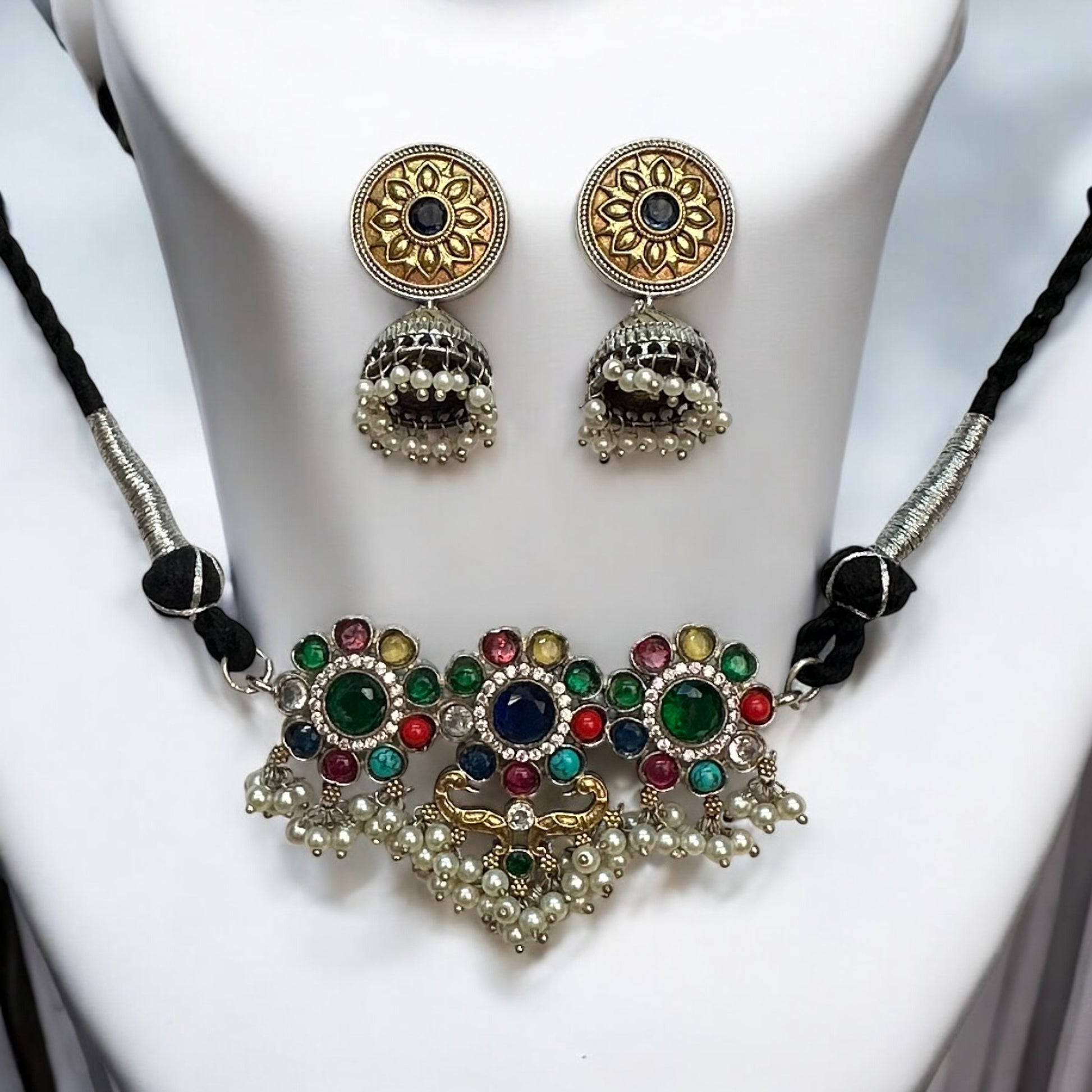 Minimal silver dual-tone choker necklace adorned with multicolor gemstones and pearl detailing, paired with intricate jhumki earrings, displayed on a white mannequin background.