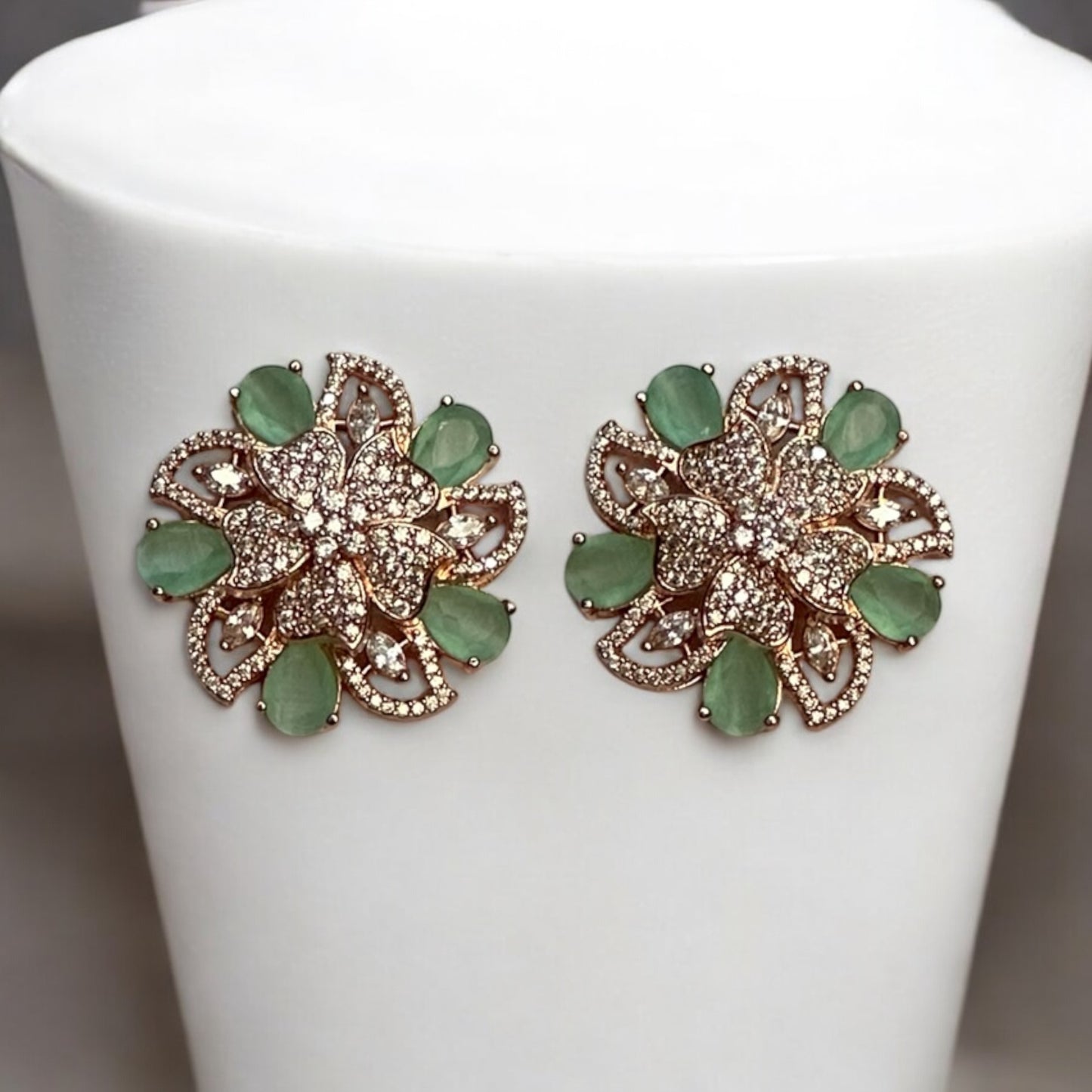 Mint green floral American diamond earrings with rose gold polish, perfect for formal and festive occasions placed on a white jewellery display stand.