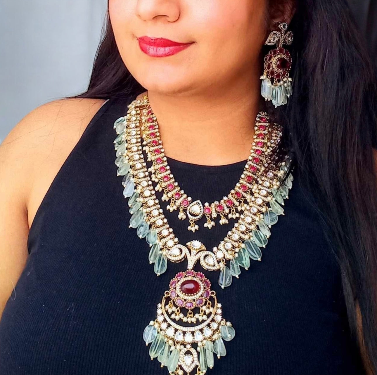 A Model in Black top displaying Elegant Royal Moissanite Polki Necklace Set Rani Haar featuring double-layered design with sparkling Moissanite, Polki stones, ruby accents, emerald-hued beads, and matching chandelier earrings. Perfect for weddings and festive occasions.