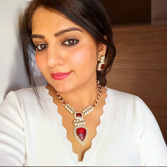 A model wearing and displaying a Real Moissanite Long Kundan Necklace set with red gemstones and matching earrings, featuring a pear-shaped pendant and intricate detailing.