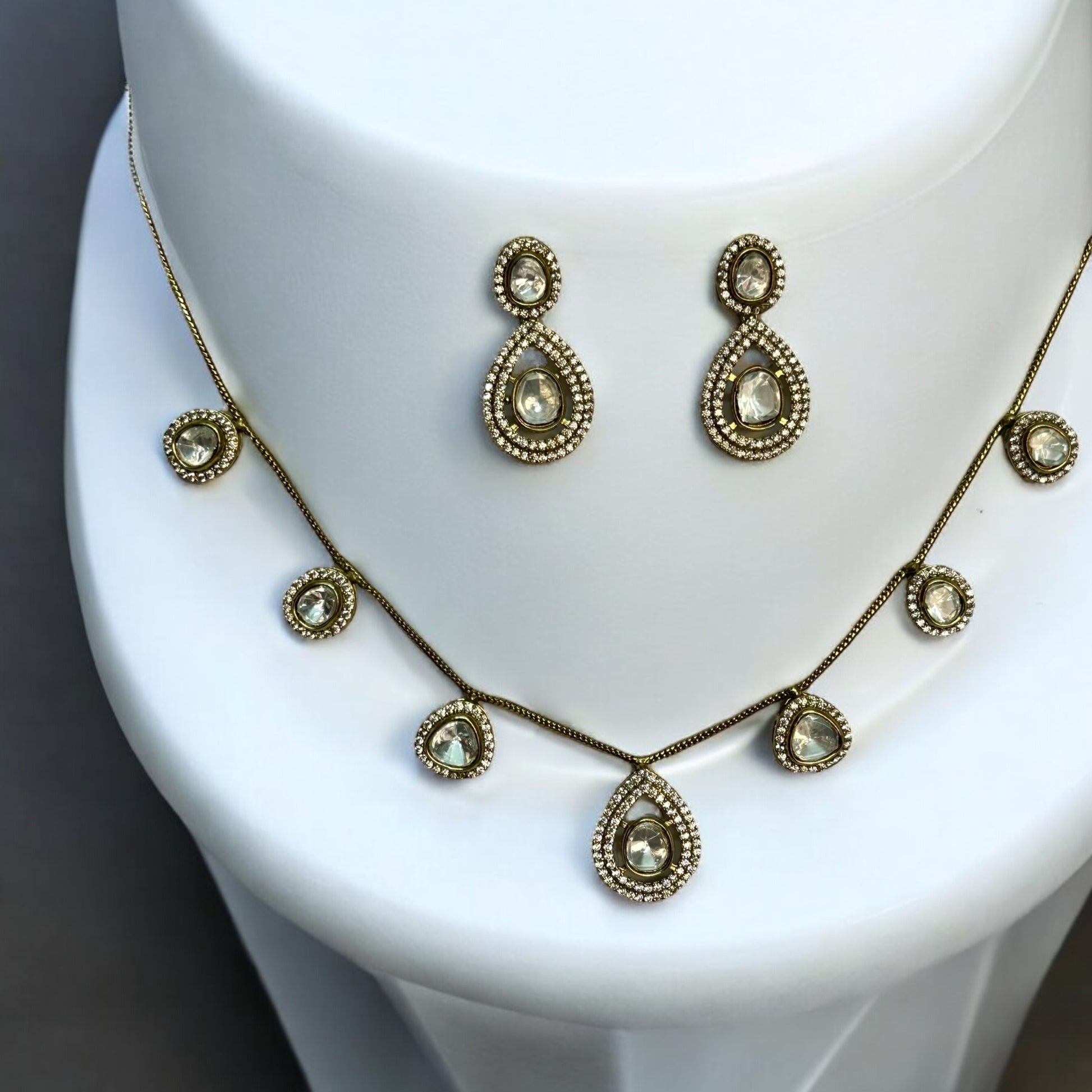 Moissanite chain design necklace set with earrings in golden colour places on a white colored jewellery display stand.
