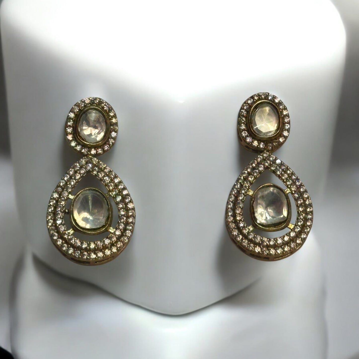 Moissanite earrings in golden colour placed on a white colored jewellery display stand.