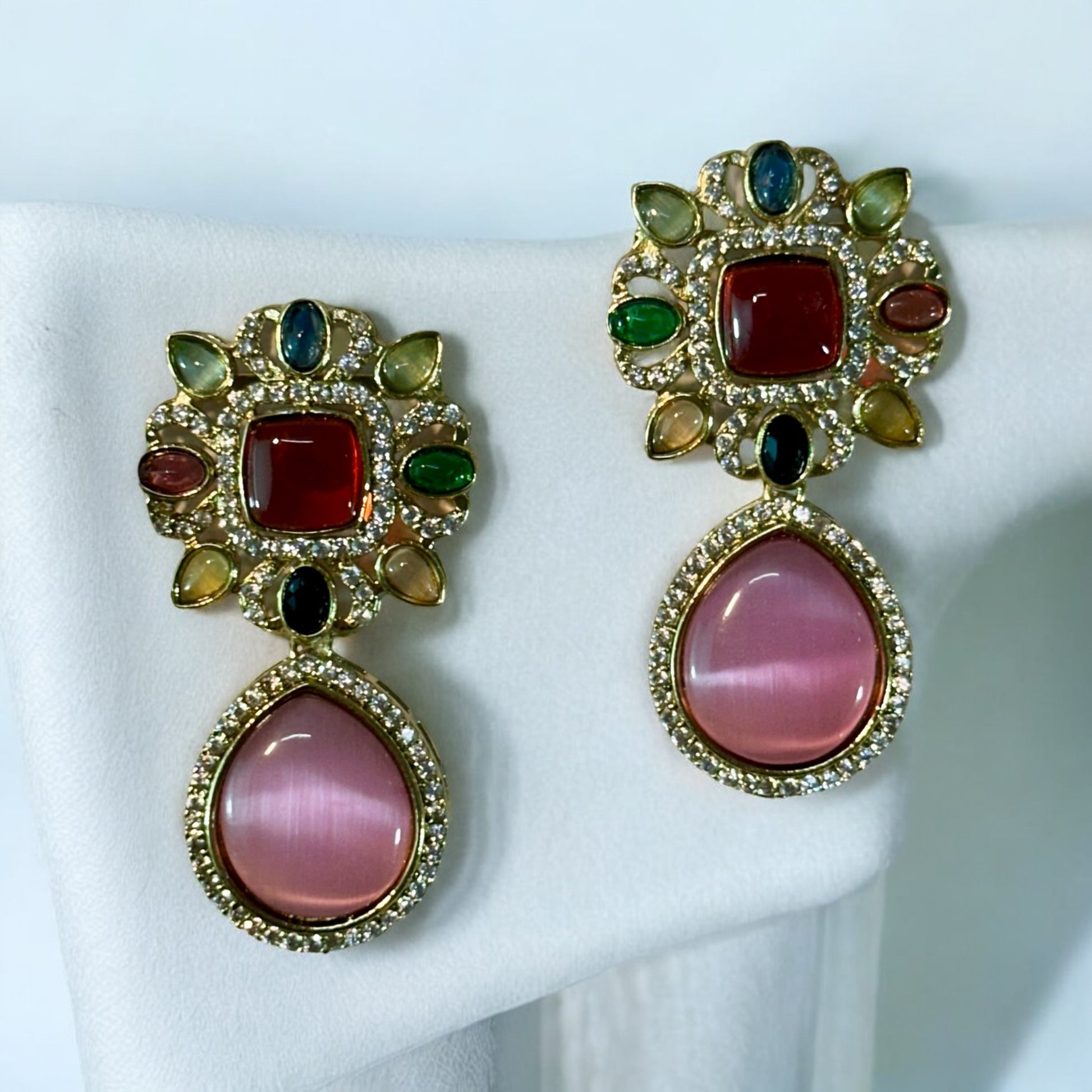 Moissanite Premium Multicolor Kundan earrings with a centred red stone and multi colored stones on its circumference with shiny crystals. It is placed on white fabric