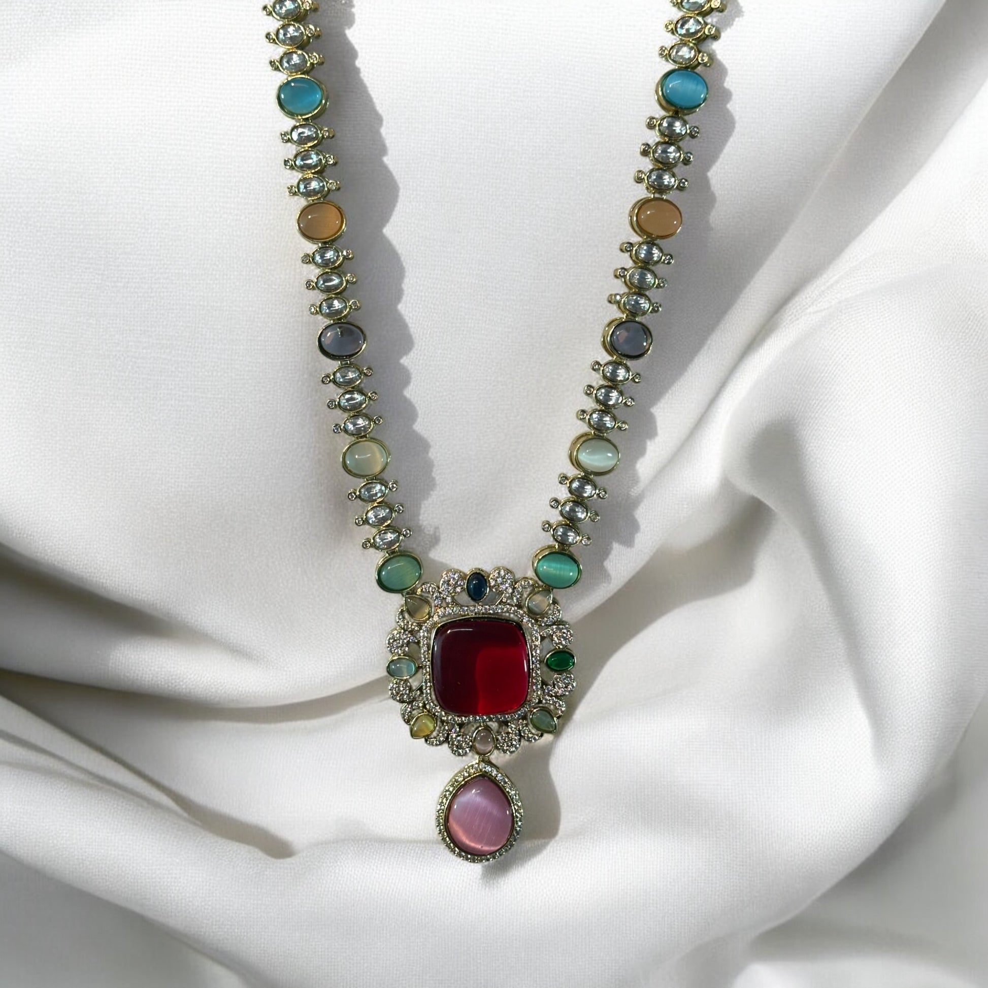 Moissanite Premium Multicolor Kundan Necklace with a centred red stone and multi colored stones on its string with shiny crystals. It is placed on white fabric