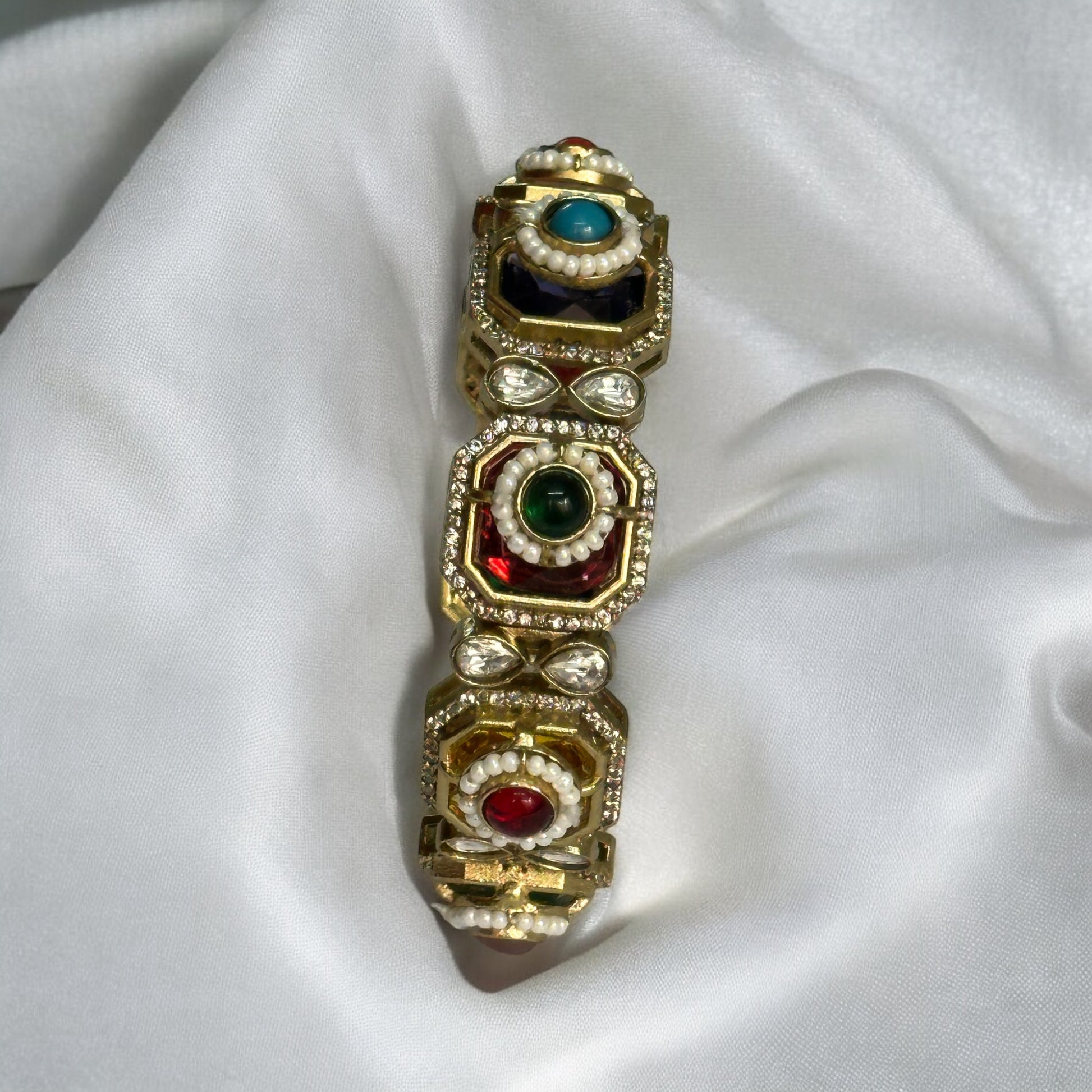 Exquisite single Pachi Kundan bangle adorned with colorful moissanite stones and delicate pearl detailing placed on a white fabric.