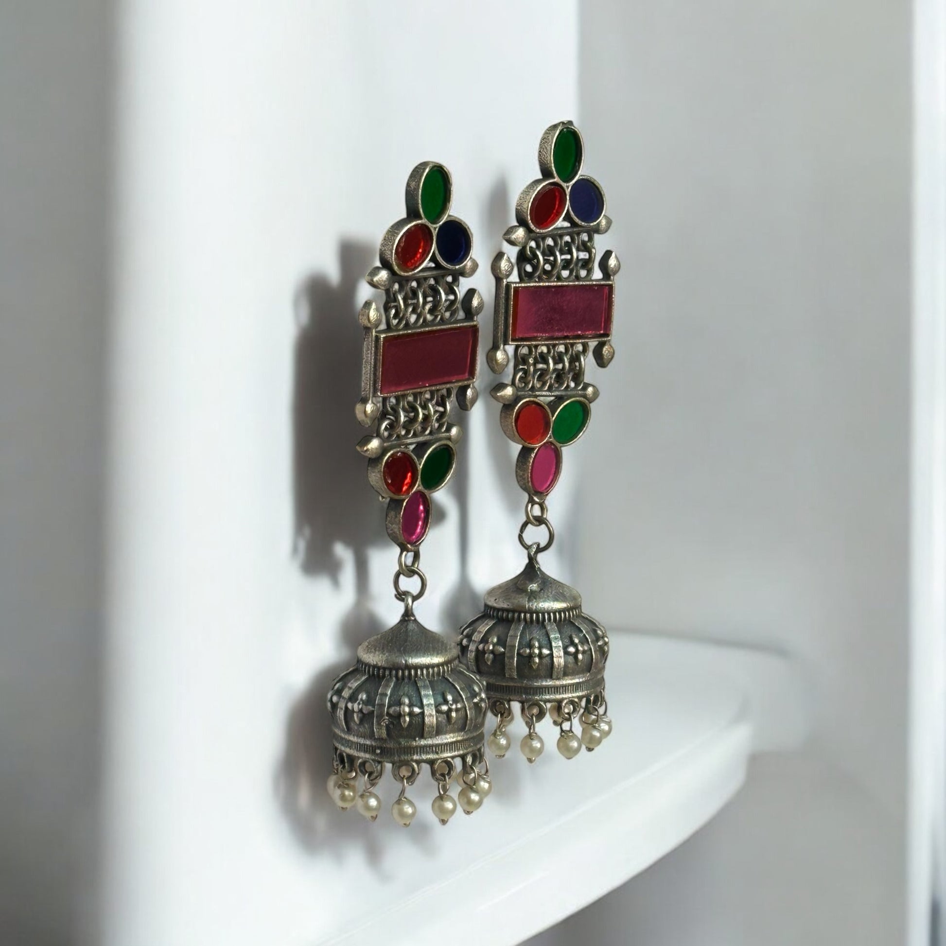 Side look if German silver earrings with colorful glass inlays in pink, green, blue, and red, featuring a jhumka design with pearl accents.