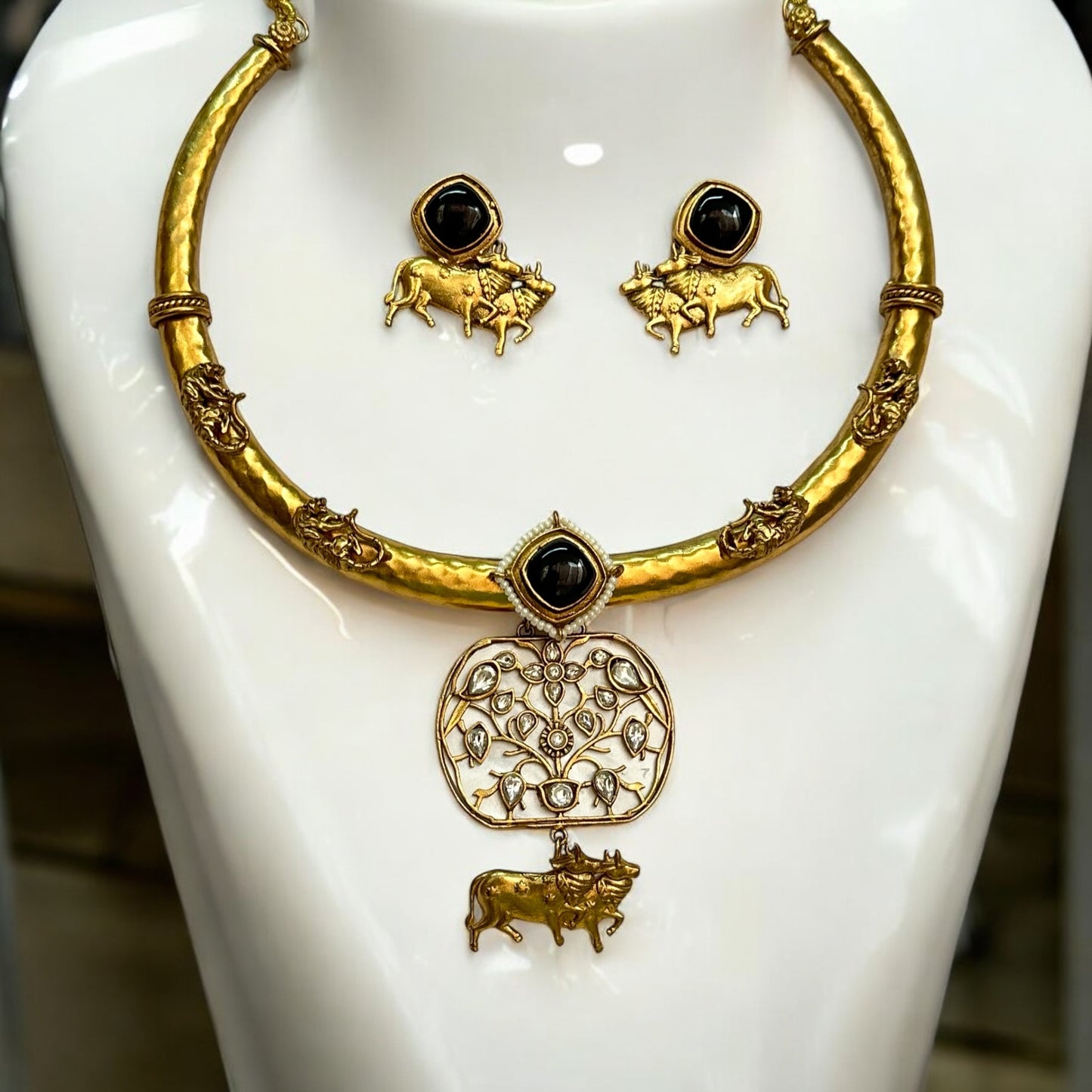 Traditional Nandi-themed Amrapali handmade hasli necklace set with intricate craftsmanship, featuring MOP accents and matching nandi designed earrings both placed on a white jewellery display stand.