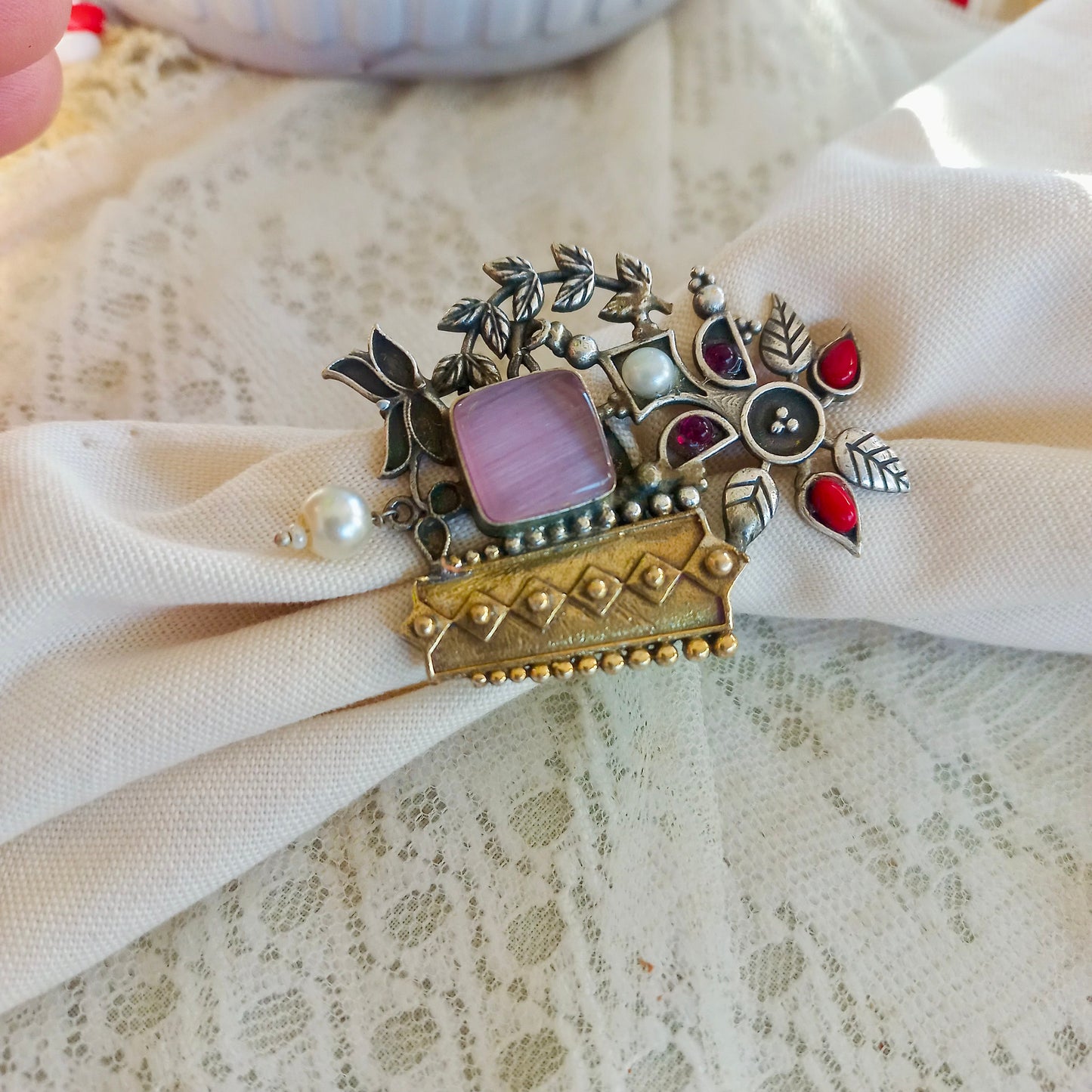 A white fabric backgroundwith an Oxidised Adjustable Fusion Ring, featuring intricate floral motifs, pearls, and a fusion of silver and gold-tone textures, perfect for a bold ethnic statement.