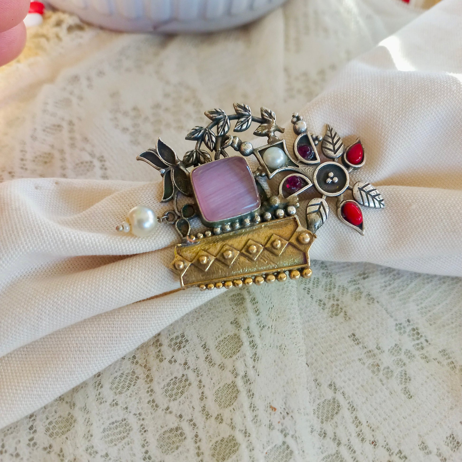 A white fabric backgroundwith an Oxidised Adjustable Fusion Ring, featuring intricate floral motifs, pearls, and a fusion of silver and gold-tone textures, perfect for a bold ethnic statement.