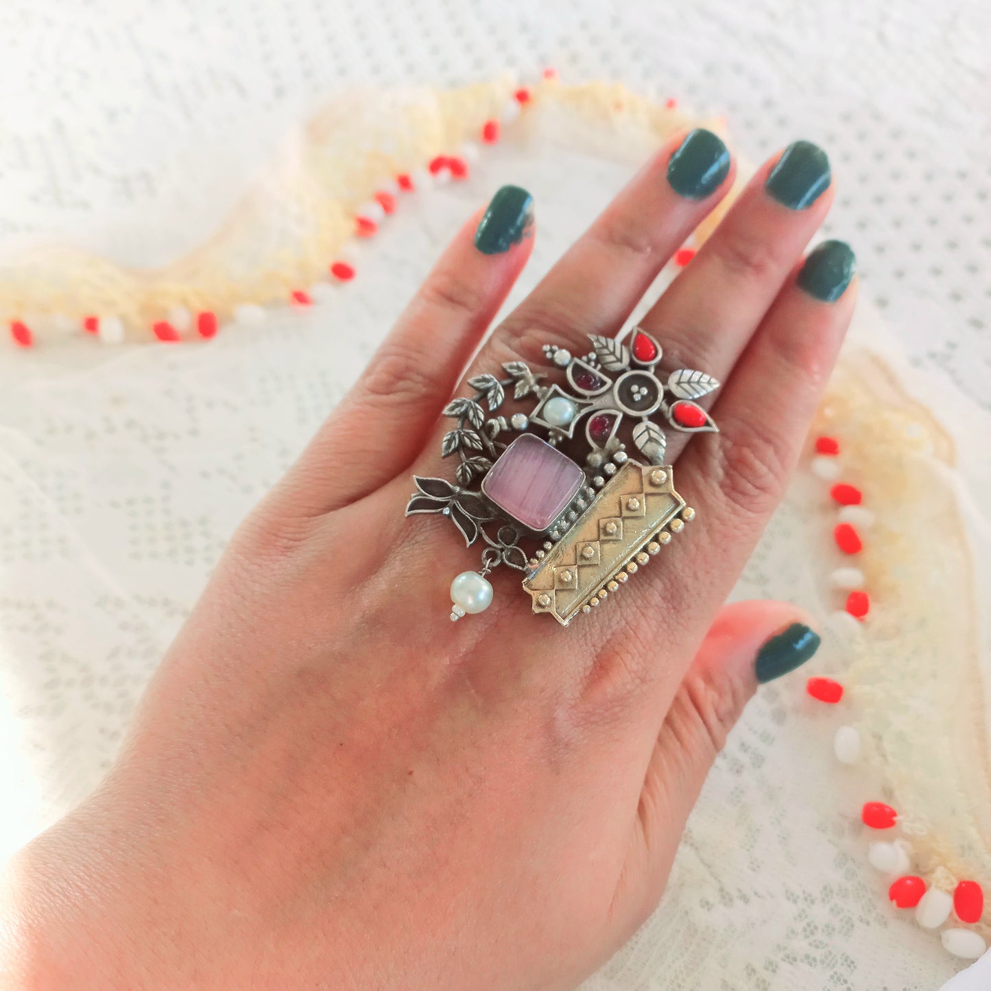 A woman's hand adorned with an Oxidised Adjustable Fusion Ring, featuring intricate floral motifs, pearls, and a fusion of silver and gold-tone textures, perfect for a bold ethnic statement.