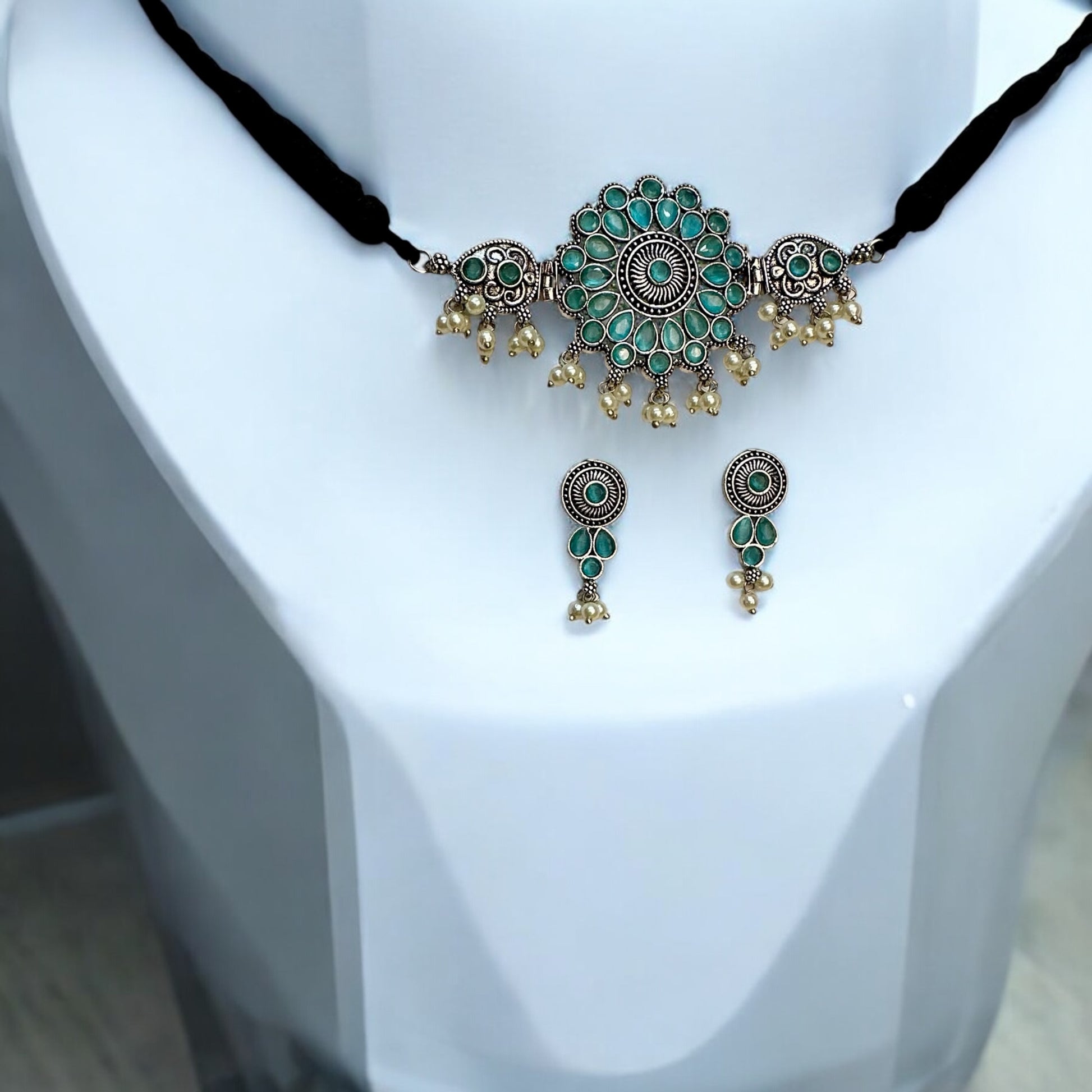 Oxidized silver choker necklace with intricate sky-blue floral designs and pearl drops. Includes matching earrings with coordinated patterns, set on a white jewellery display stand.
