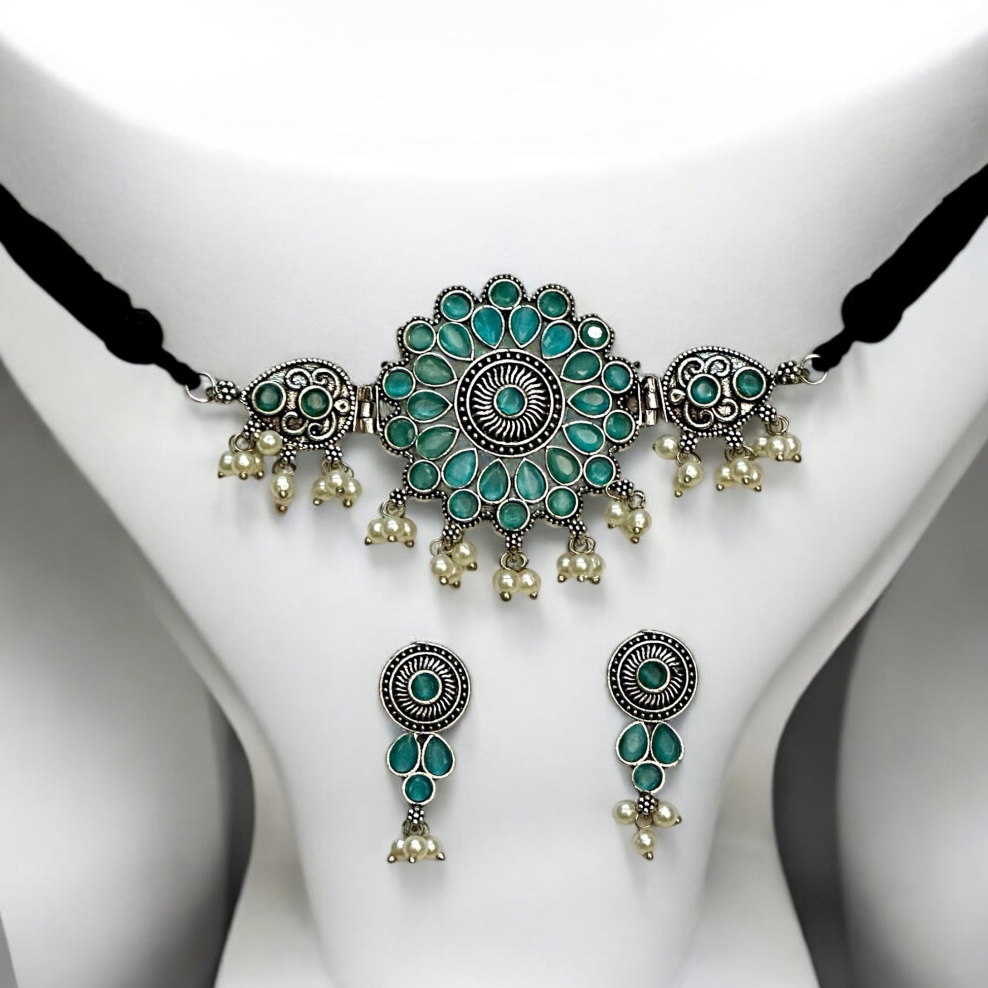 Oxidized silver choker necklace with intricate sky-blue floral designs and pearl drops. Includes matching earrings with coordinated patterns, set on a white bust display.