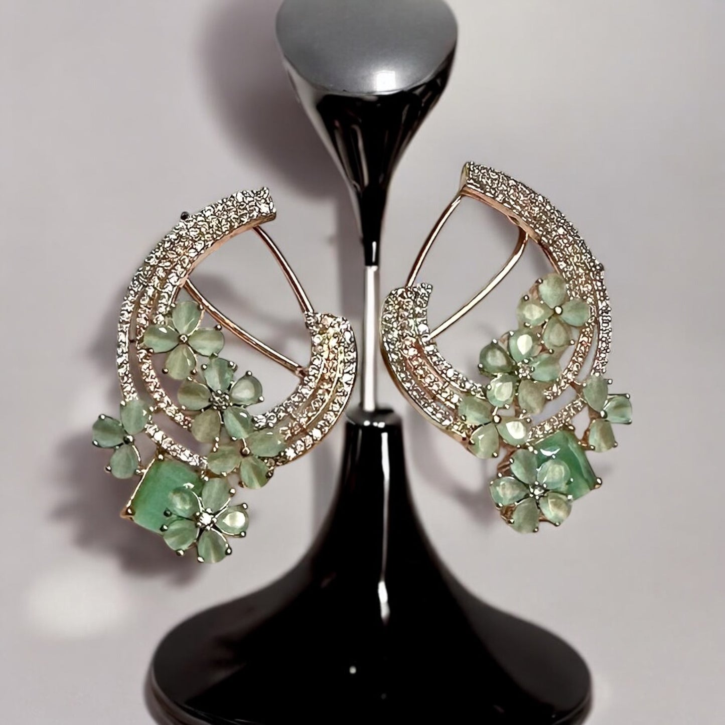 Partywear Statement American Diamond Earrings – crescent-shaped design with mint floral accents, gemstones, and layers of American diamonds. It is placed on a black jewellery display stand. Ideal for festive and formal occasions.