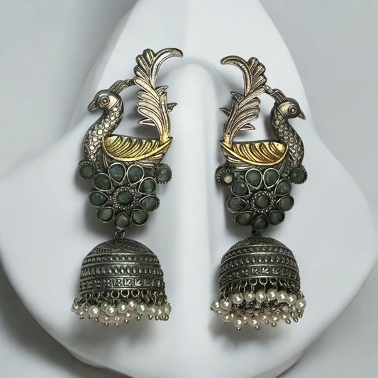 Dual-tone peacock jhumka earrings with floral stone detailing and pearl drops displayed on white – Bella & Diva
