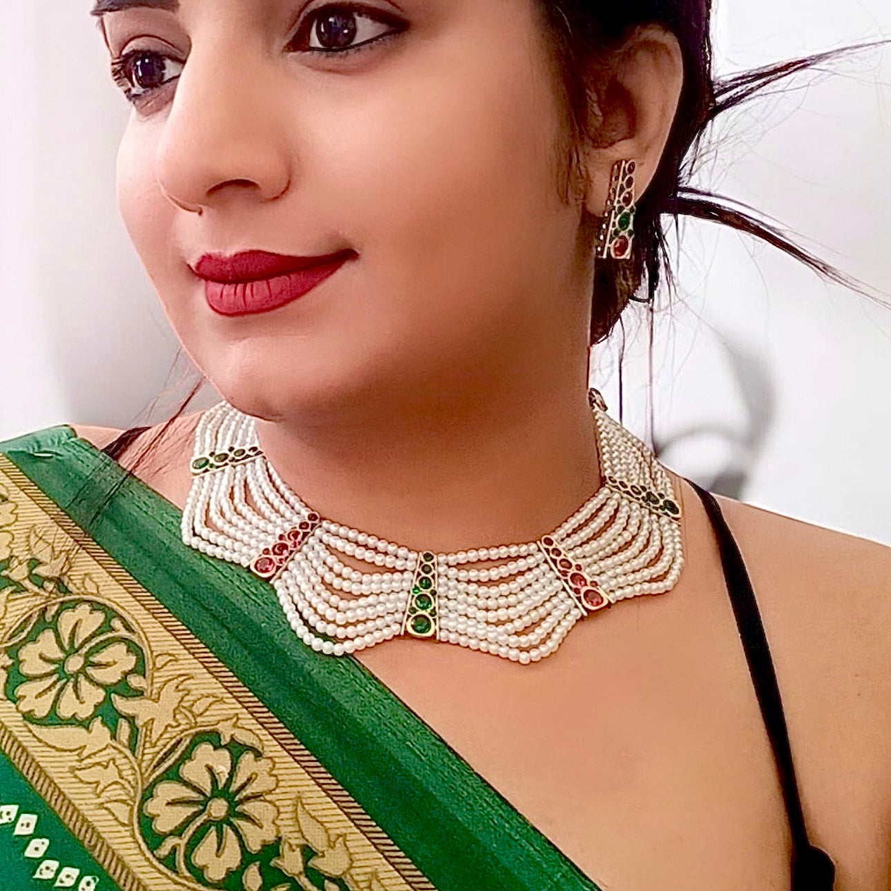 A model displaying and wearing a Elegant pearl necklace and earrings set with red and green stone accents, perfect for festive and traditional occasions.
