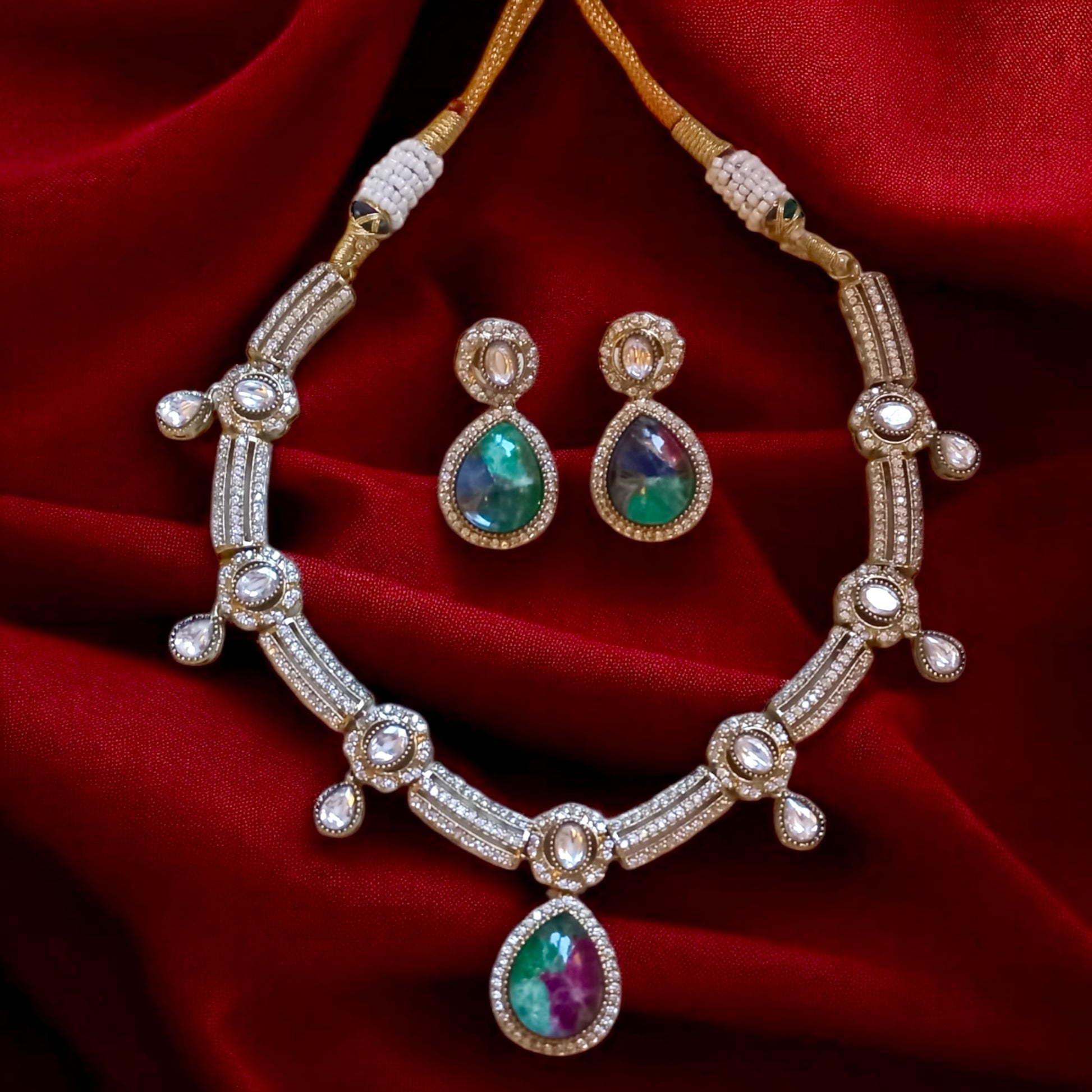 Premium moissanite necklace set with green and ruby multi-colour doublet stones and matching earrings, placed on red satin fabric