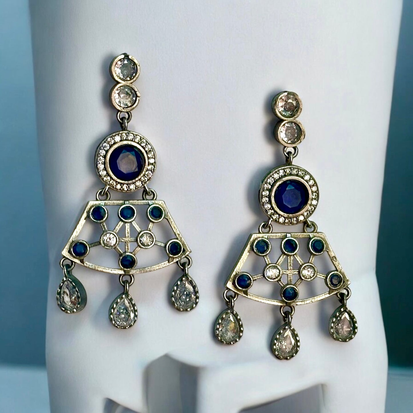 Premium Silver look a like statement earrings in silver and navy blue color stoned placed on a white coloured jewellery display stand.