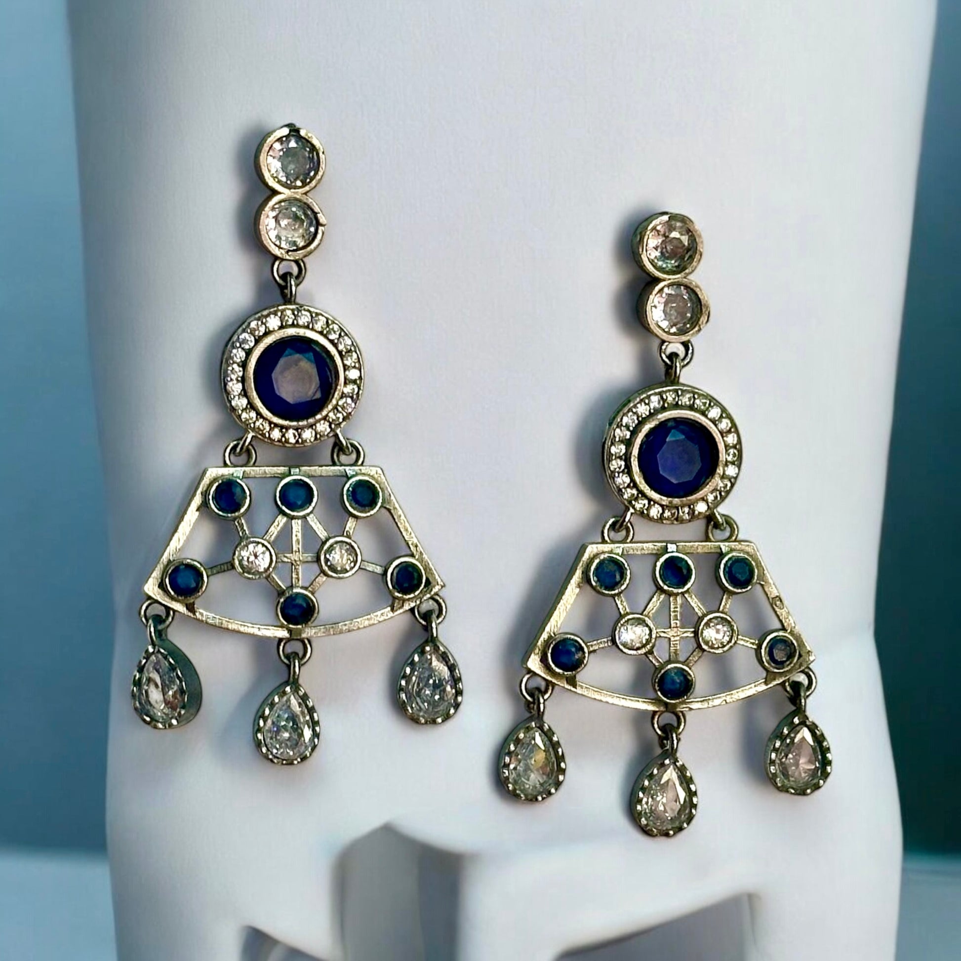 Premium Silver look a like statement earrings in silver and navy blue color stoned placed on a white coloured jewellery display stand.