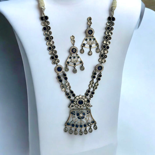 Premium Silver look a like statement necklace and earrings in silver and navy blue color stoned placed on a white coloured jewellery display stand.