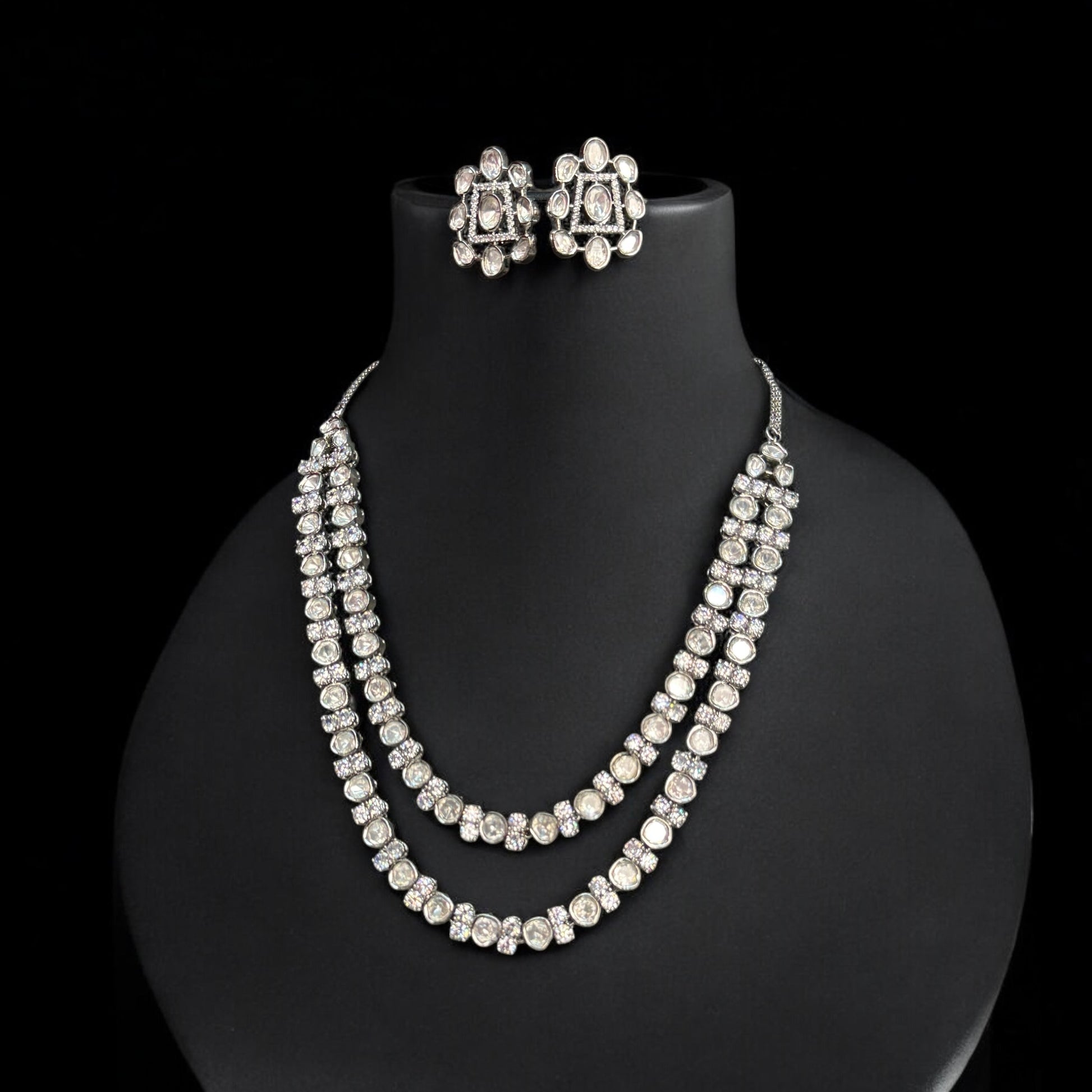 Premium Tyani Kundan double-layer necklace with sparkling stones and matching oversized stud earrings, crafted for luxury occasions. It is placed on a black jewellery display stand.