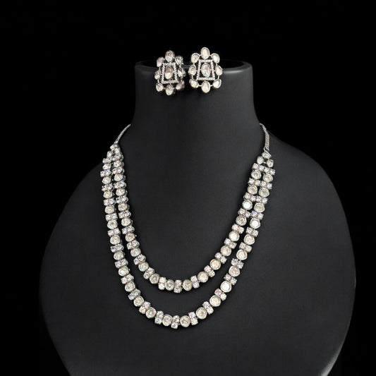 Premium Tyani Kundan double-layer necklace with sparkling stones and matching oversized stud earrings, crafted for luxury occasions. It is placed on a black jewellery display stand.