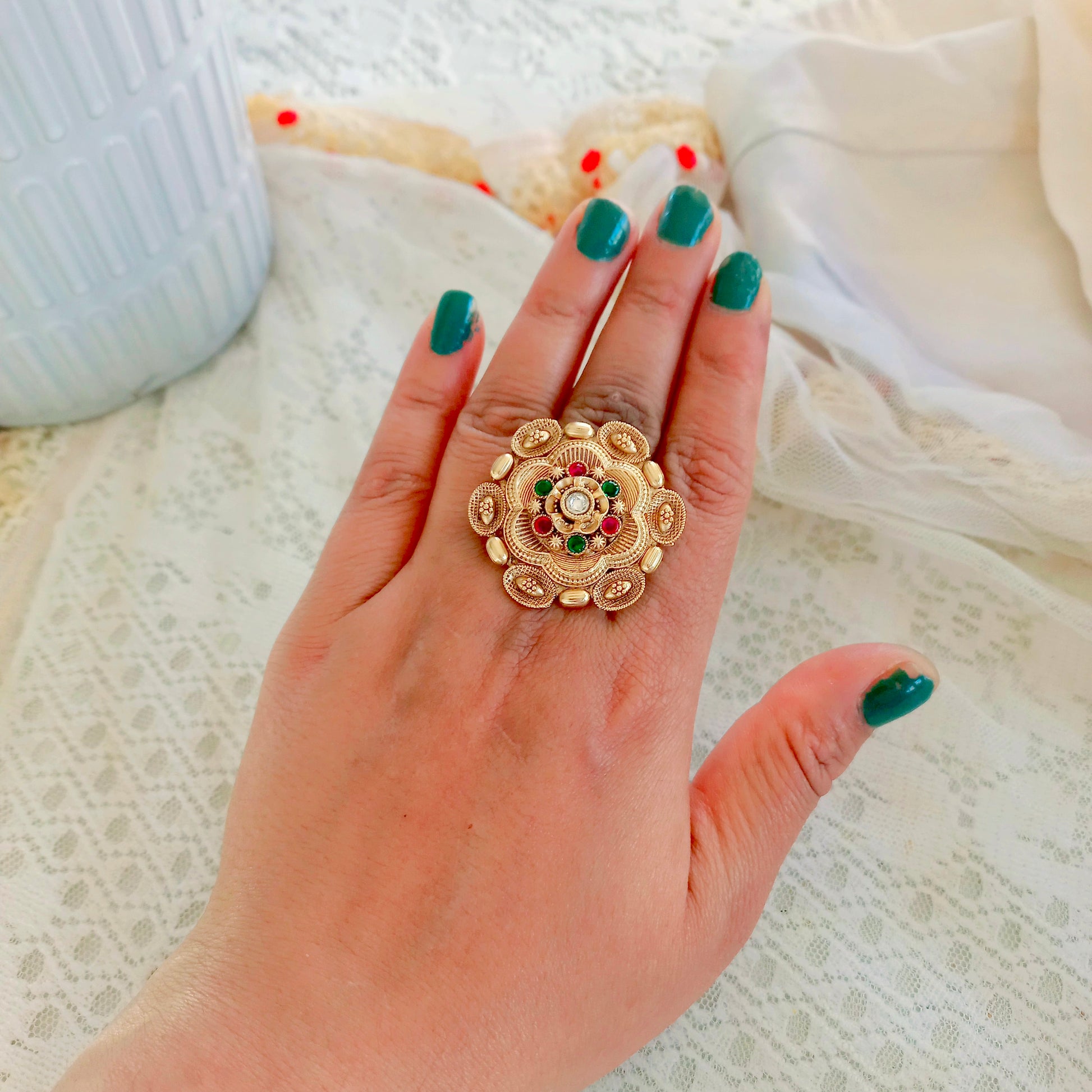A woman's hand showcasing a Rajwadi Multicolor Golden Finger Ring with intricate floral design, gold-toned finish, and multicolor stone embellishments, exuding traditional festive elegance.

