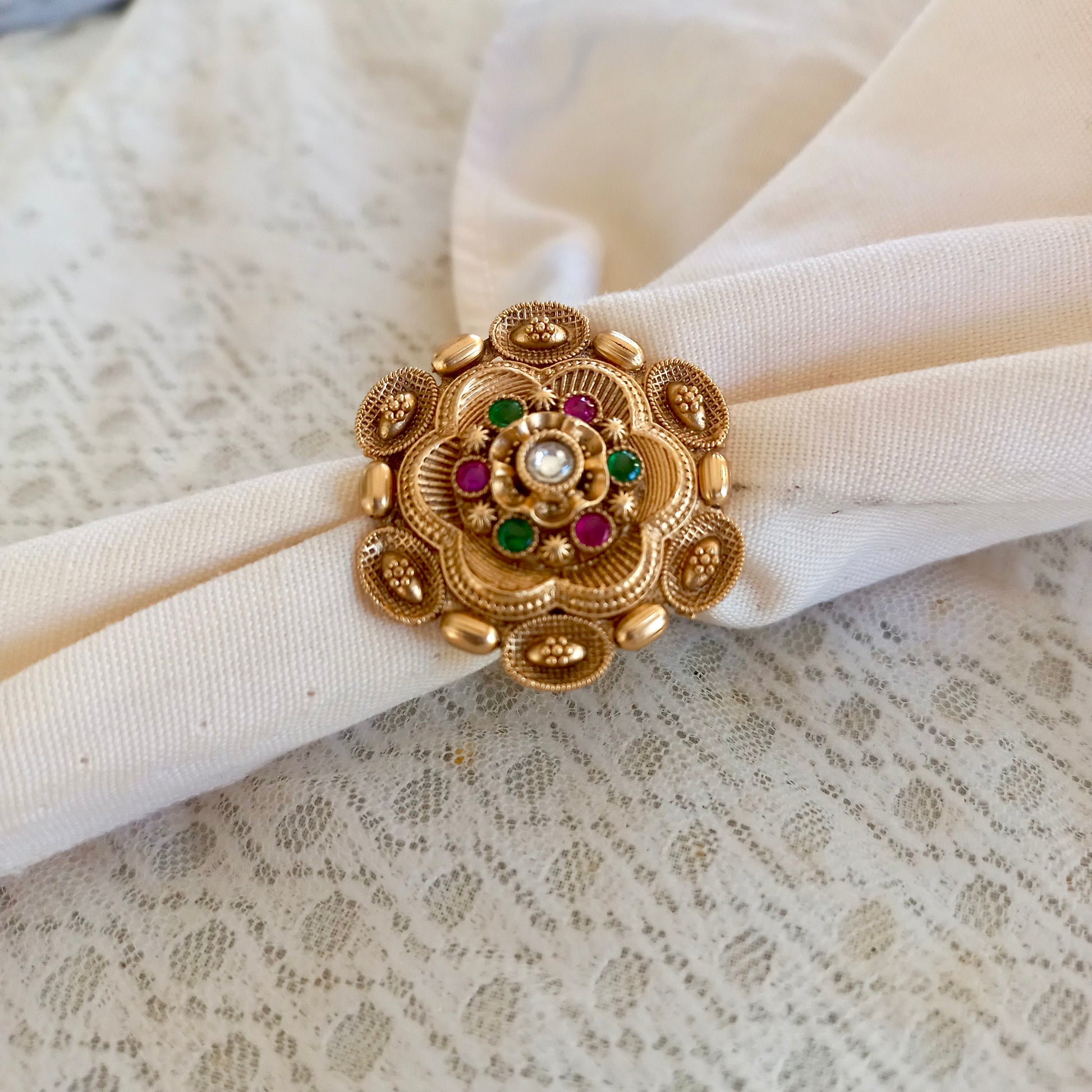 A white fabric background showcasing a Rajwadi Multicolor Golden Finger Ring with intricate floral design, gold-toned finish, and multicolor stone embellishments, exuding traditional festive elegance.