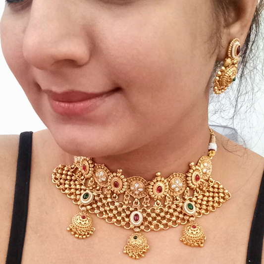 A Model wearing a Golden Rajwadi Kundan choker necklace set with intricate detailing, red and green gemstone accents, and matching earrings.
