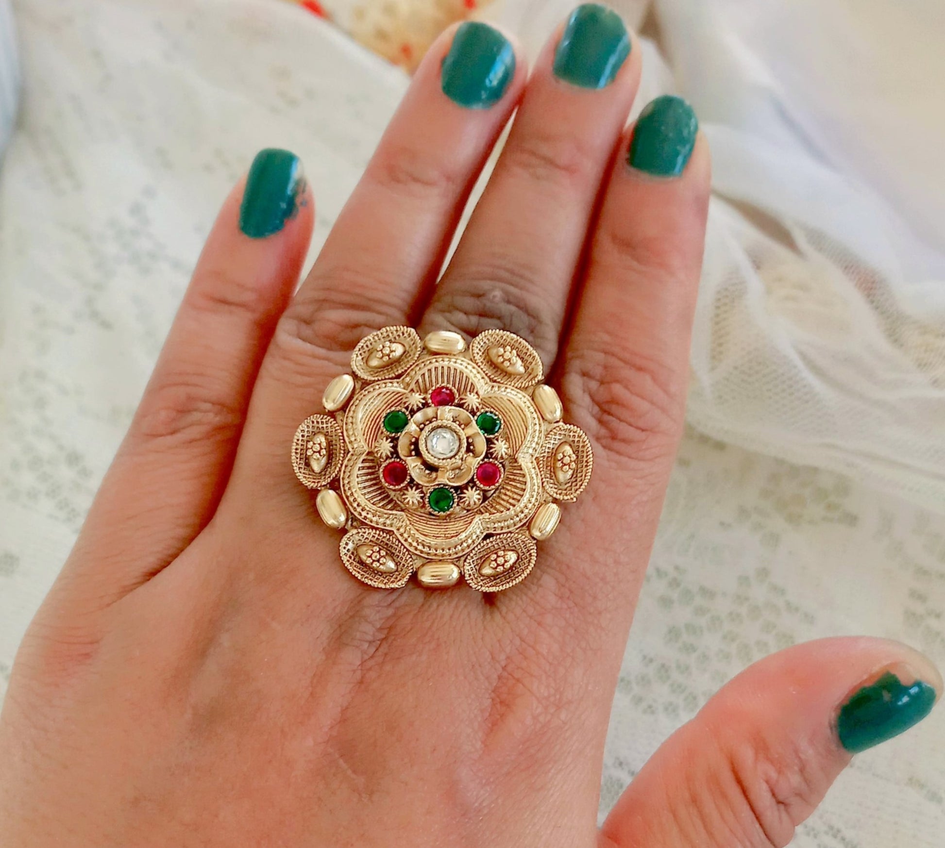 A woman's hand showcasing a Rajwadi Multicolor Golden Finger Ring with intricate floral design, gold-toned finish, and multicolor stone embellishments, exuding traditional festive elegance.