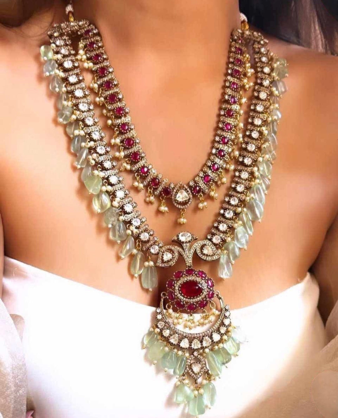 A model displaying Elegant Royal Moissanite Polki Necklace Set Rani Haar featuring double-layered design with sparkling Moissanite, Polki stones, ruby accents, emerald-hued beads, and matching chandelier earrings. Perfect for weddings and festive occasions.